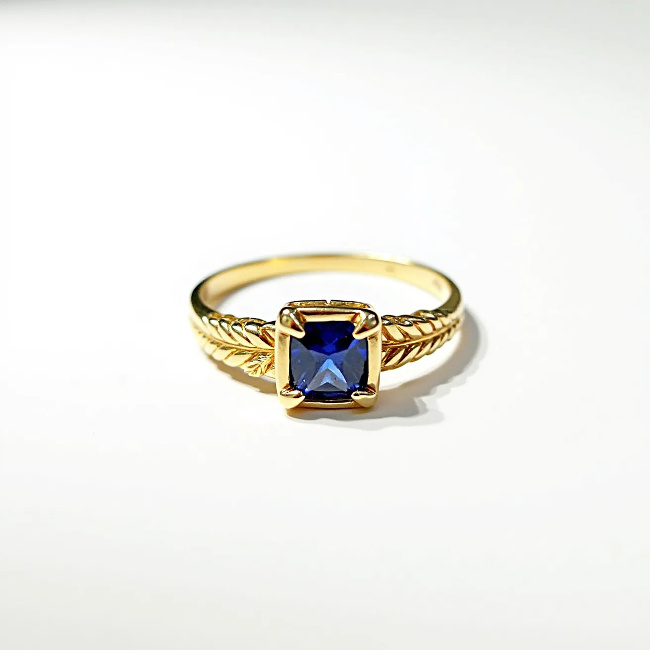 This Solomon's ring features a beautifully crafted band in a gold material, with a striking design that includes a twisted, rope-like pattern. At its center, the ring showcases a deep blue square-cut gemstone, likely a sapphire, held securely in place by a four-prong setting that provides stability and emphasizes the gem’s brilliance. The combination of the intricate band design with the vibrant gemstone accentuates the ring’s regal aesthetic.