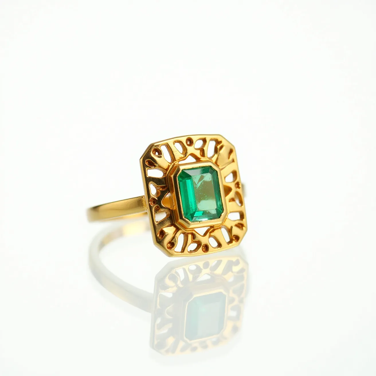 This square ring features a vibrant rectangular green gemstone, likely an emerald, centrally positioned and cut with precision. The stone is set in an openwork gold setting, highlighting an elaborate design that combines elegance and intricacy. The metal appears to be gold, offering a classic and luxurious appearance, complemented by the symmetrical craftsmanship of the surrounding lattice. The band is smooth and polished, seamlessly integrating with the ornate top without any visible clasp or additional attachment, emphasizing a sophisticated and unified design.