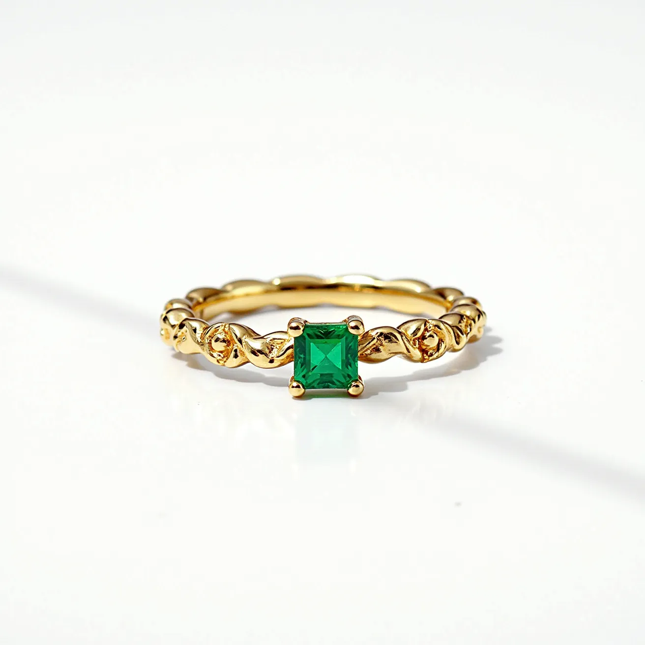 This square ring features an intricately designed gold band with a twisted pattern that adds a touch of elegance. At its center lies a striking green gemstone, likely an emerald or similar stone, cut into a square shape and set in a prong setting that secures it firmly in place. The prong setting accentuates the stone’s brilliance and ensures maximum visibility, highlighting the vivid green color. The gold band appears polished and well-crafted, complementing the gemstone's hue beautifully. The ring's design seamlessly combines a classic look with a modern twist, making it a standout piece of jewelry.