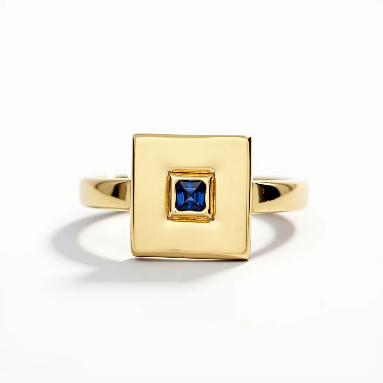 This square ring features a gold band and a prominent square top plate. At its center is a square-cut blue gemstone, likely a sapphire, which is securely set into the gold, possibly using a bezel setting that highlights its vibrant color. The ring's sleek design emphasizes the contrast between the rich gold and the deep blue of the stone, creating an elegant and modern aesthetic without the need for additional clasps or attachments.