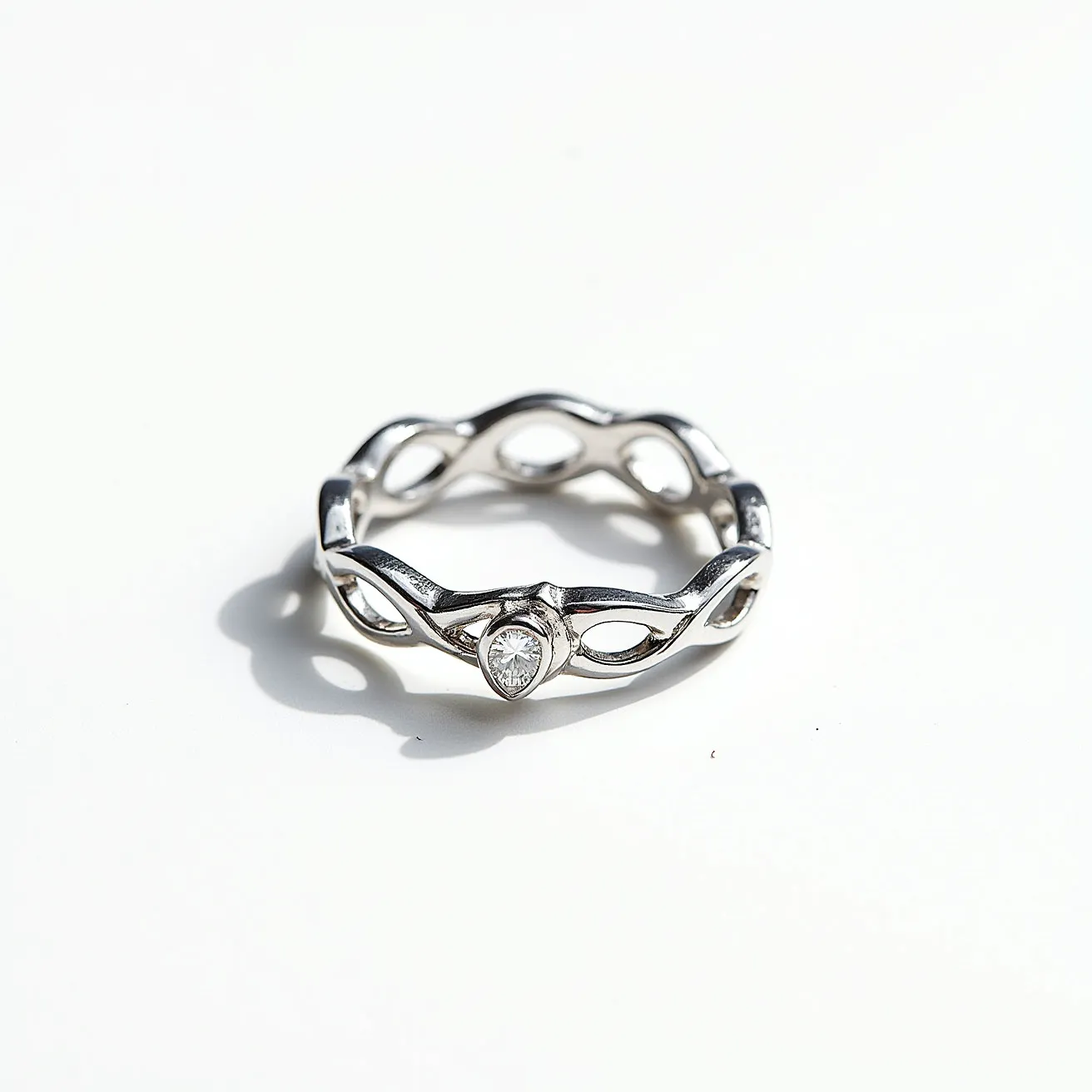 This stackable diamond ring features a contemporary design crafted from a polished metal, likely silver or white gold, forming an interwoven, open band structure. At its center, the ring is adorned with a single round cut diamond, securely set in a bezel setting, which provides a sleek and modern look while highlighting the stone’s brilliance. The absence of any visible clasps or attachments emphasizes the seamless and continuous design of the piece, making it ideal for stacking with other rings to create a personalized style statement.