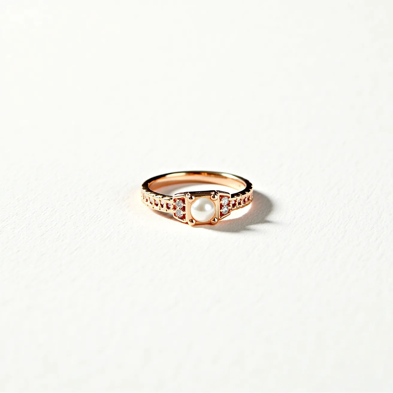 This stackable diamond ring is crafted from rose gold, featuring a central round pearl set prominently within an elegant bezel setting. Flanking the pearl on either side are small round diamonds, adding a touch of brilliance and complementing the central gem. The band itself is adorned with a series of small, channel-set diamonds, enhancing the ring's sparkle and adding texture to the design. The combination of the lustrous pearl with the sparkling diamonds and the warm hue of rose gold creates a refined and versatile piece suitable for stacking with other rings.