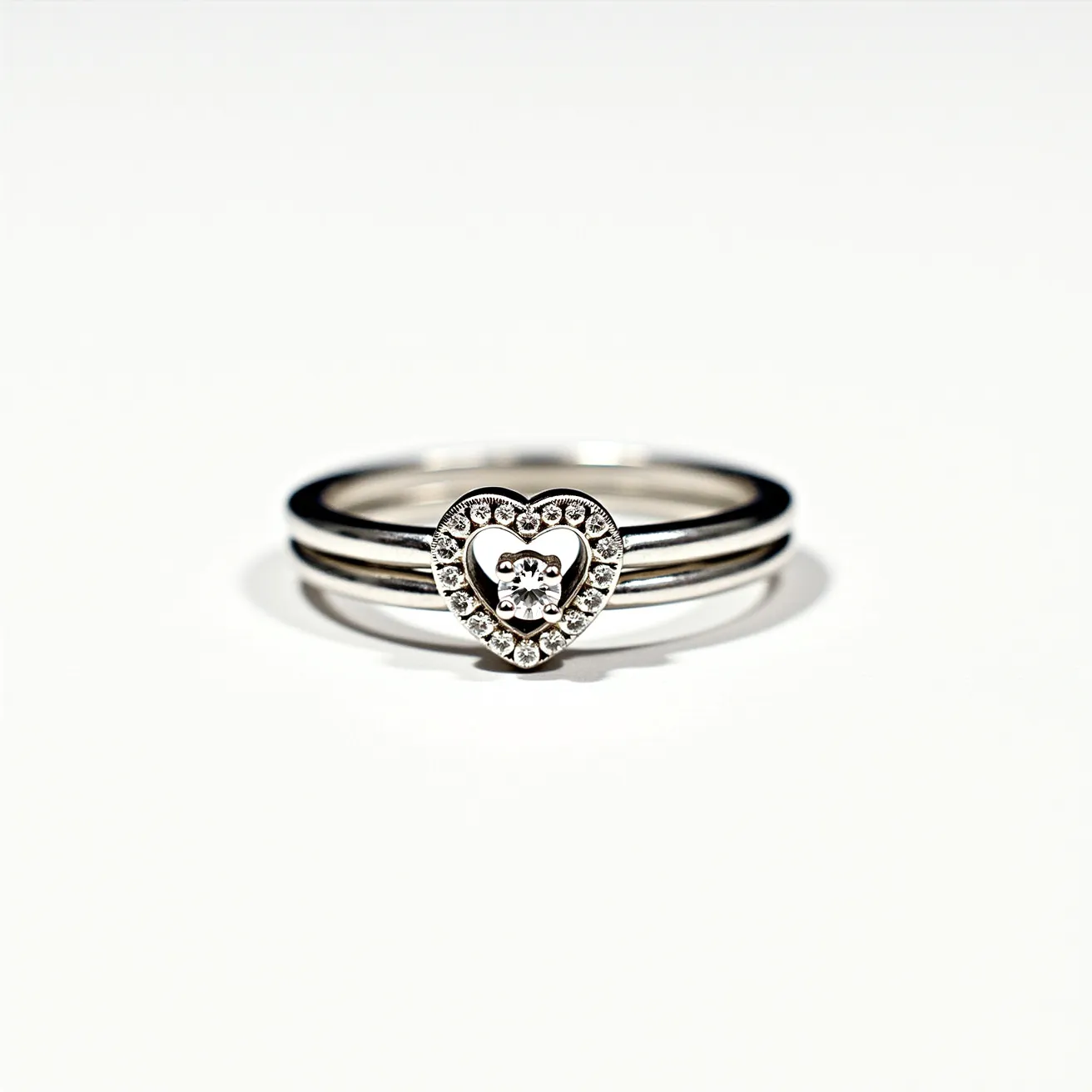 This stackable engagement ring features a delicate heart-shaped design crafted from a shiny metal, likely white gold or platinum, that forms the foundation for its stackable bands. The focal point is a central, round-cut diamond set within the middle of the heart, which is surrounded by smaller accent diamonds that form a sparkling halo. These smaller stones are meticulously placed in a pavé setting, enhancing the ring's brilliance without an overwhelming appearance. The design allows for stacking, offering versatility and personalization to the wearer.