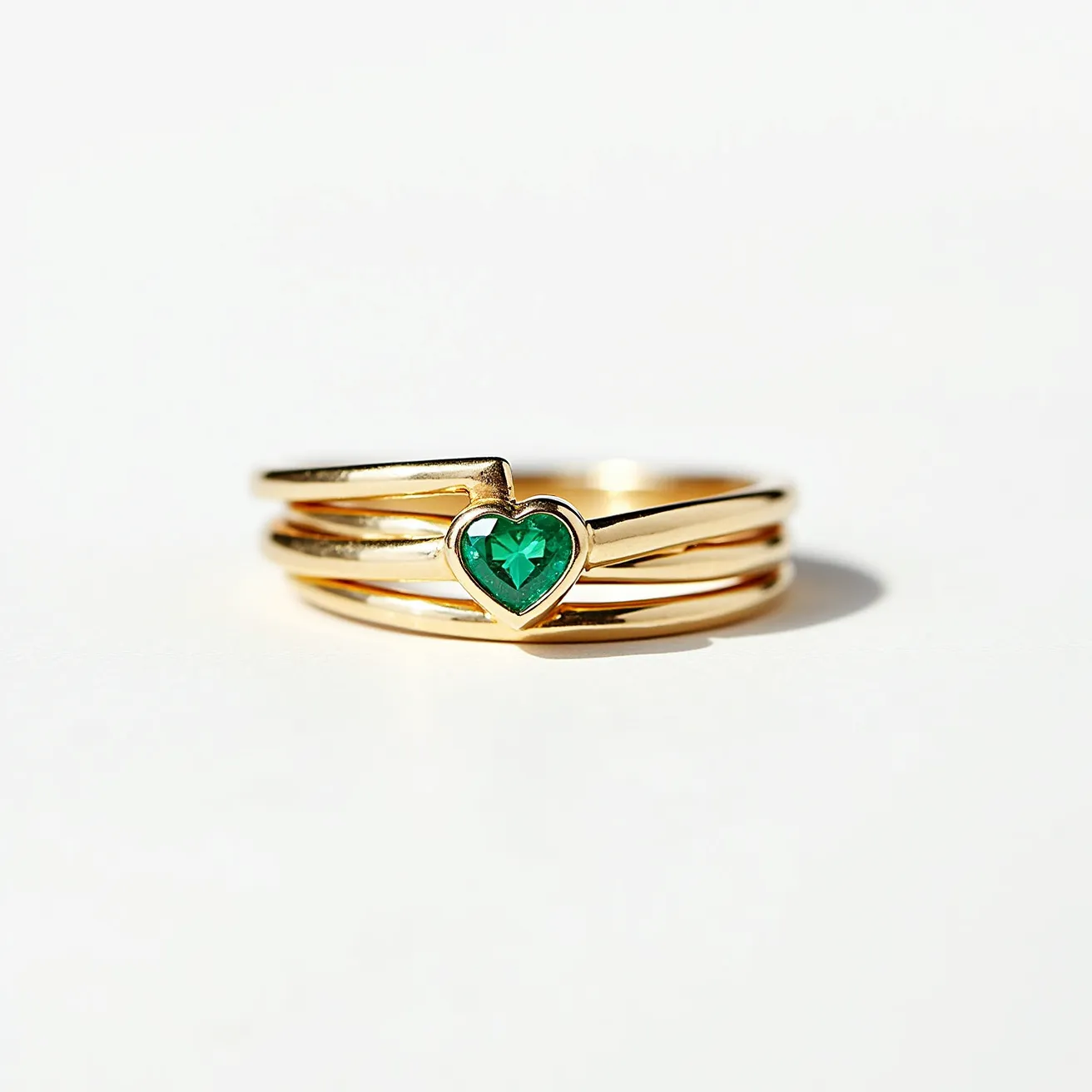 This stackable mothers ring features a sleek, polished gold band composed of multiple interlaced rings. At its center, the design showcases a vibrant heart-shaped green gemstone, securely set within a bezel setting. The elegant combination of the gold band and the vivid green stone creates a harmonious aesthetic, highlighting the sentimental value typically associated with mothers rings.