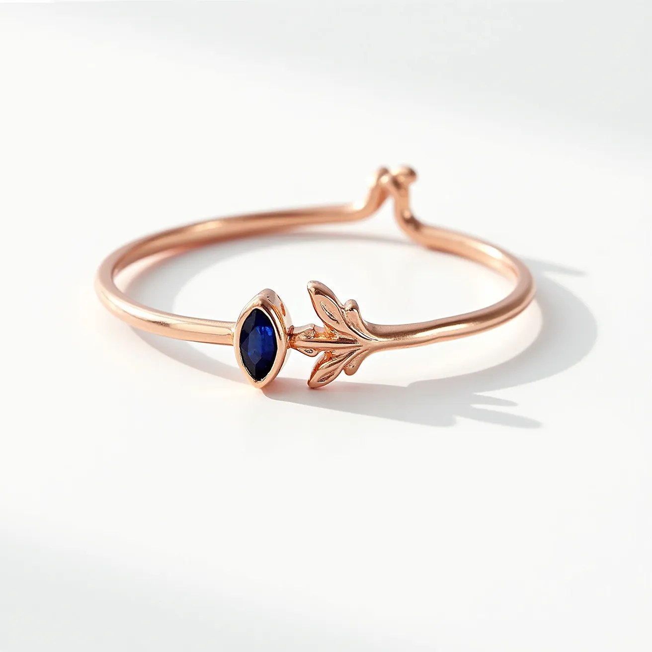 This stackable mothers ring showcases a delicate and elegant design crafted from rose gold, giving it a warm and sophisticated appearance. It features a marquise-cut blue gemstone, likely a sapphire or similar stone, prominently set in a bezel setting, ensuring both security and style. The ring also includes a unique leaf motif, adding a natural and personalized touch. The sleek band is shaped to allow multiple rings to be worn together, enhancing its versatility and symbolic meaning.