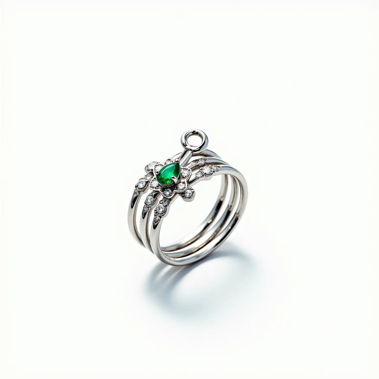 This stackable mothers ring is crafted from a polished silver-toned metal, featuring a stunning assembly of three interconnected bands. At its centerpiece, a striking pear-cut green gemstone is set, surrounded by a floral arrangement of small, round, clear stones, likely diamonds, enhancing its elegance. The green gemstone is securely held in a prong setting, ensuring its prominence and stability. Atop the floral design, an attached small loop adds an intricate element to the ring’s design, possibly for attaching a charm. The combination of vibrant colors with classic metallic tones makes this ring both modern and timeless.