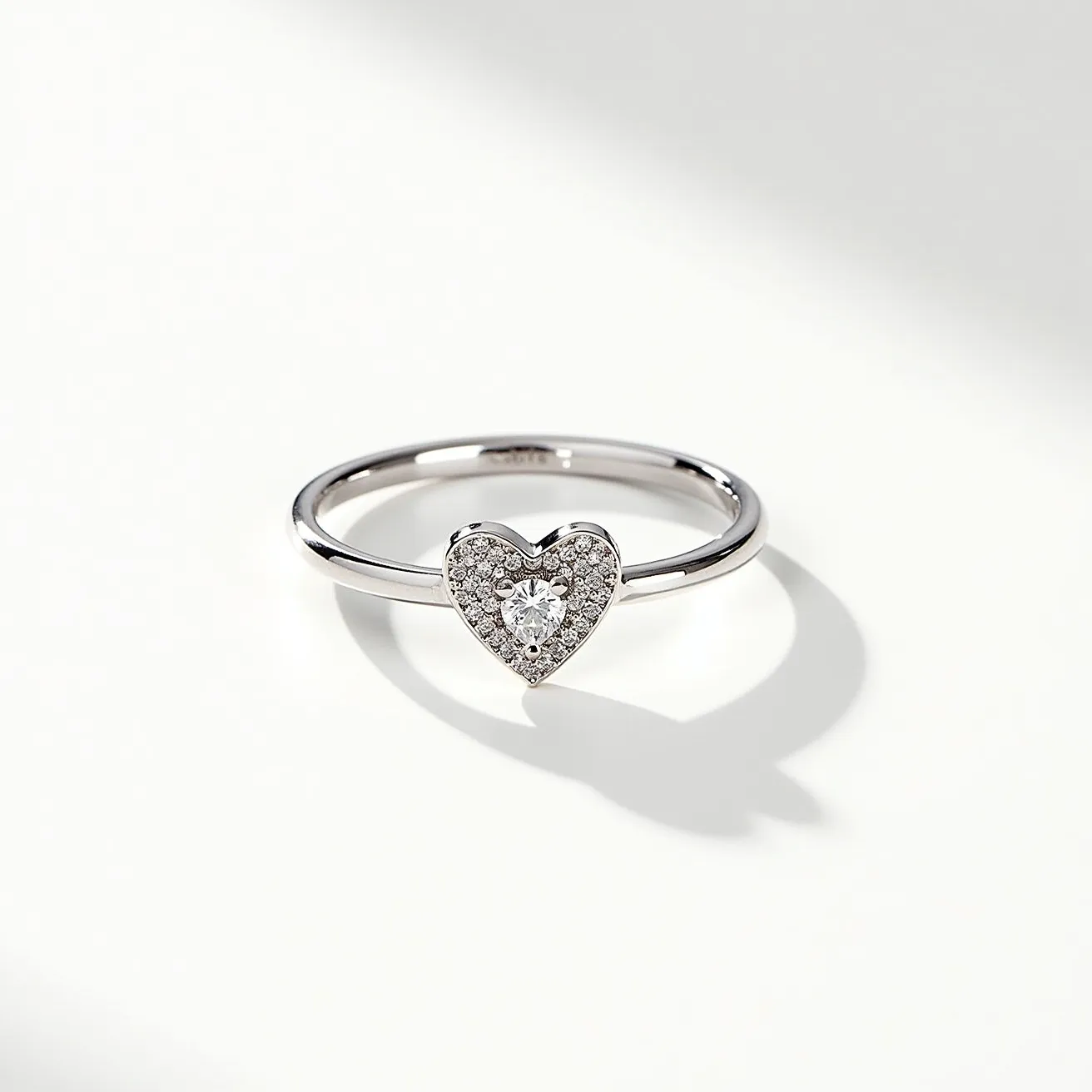 This stackable mothers ring features a sleek, polished metal band, likely crafted from white gold or platinum, providing a lustrous and timeless finish. The focal point of the ring is a heart-shaped setting adorned with a central round-cut diamond, exuding brilliance and elegance. Surrounding the central gem, numerous smaller diamonds are meticulously pavé-set, enhancing the overall sparkle and adding intricate detail to the heart design. The absence of additional clasps or attachments emphasizes the ring's streamlined and elegant design, making it ideal for wearing alone or stacked with other rings.