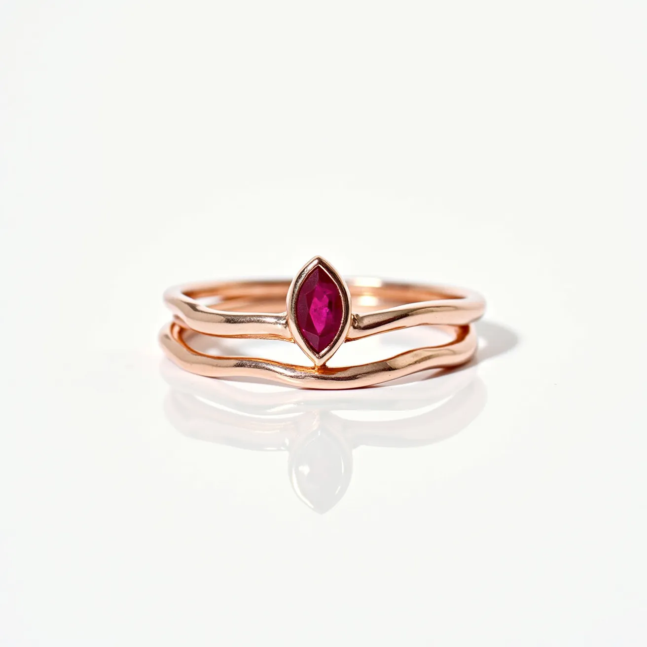 These stackable rings are crafted from a warm-toned metal, likely rose gold, with a fluid, organic design that allows them to seamlessly interlock. The focal point is a marquise-cut gemstone, likely a ruby, set in a secure bezel setting that highlights its vibrant red hue. The rings exhibit a smooth, polished finish, enhancing the lustrous appearance of the metal and providing an elegant contrast with the stone's deep color. There is no clasp or additional attachment, allowing for a versatile and understated elegance suitable for various occasions.