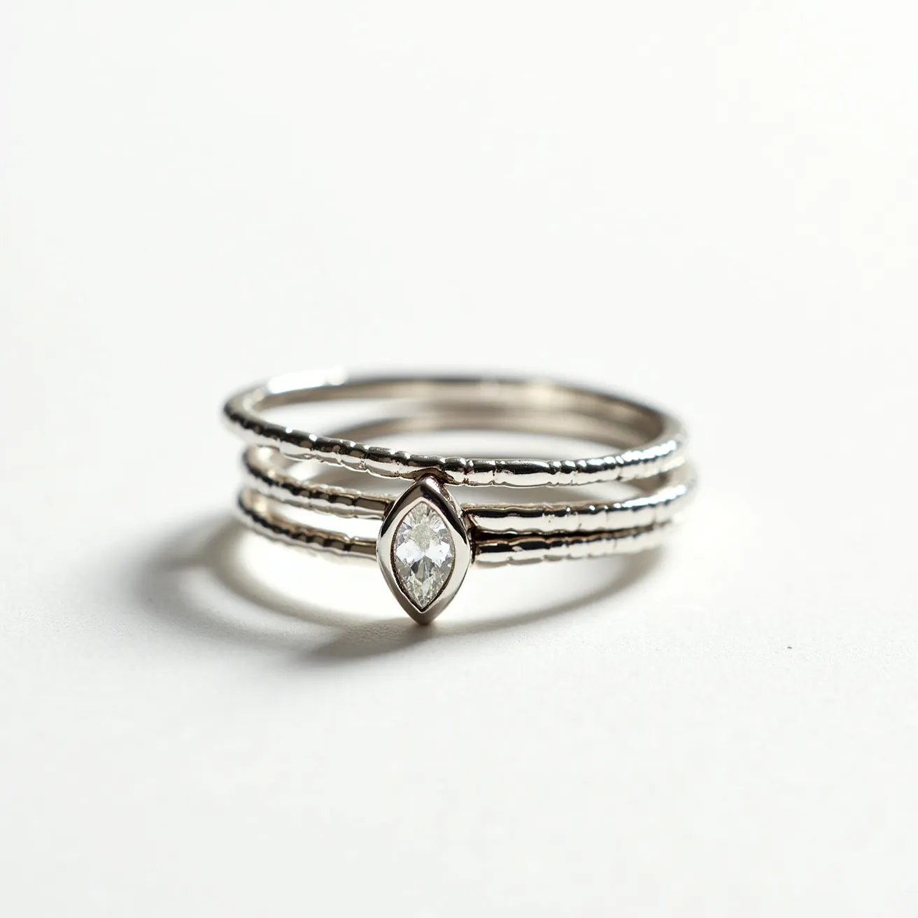 These stackable rings are crafted from a glossy metal that suggests a silvery material, possibly sterling silver or white gold, and feature a minimalist design with a delicate texture along the bands. Central to the design is a singular, marquise-cut gemstone, set in a bezel-style setting that securely holds the stone while allowing its shape and facets to catch the light. The rings do not appear to have any additional clasps or attachments, relying instead on their stackable nature for versatility and style.