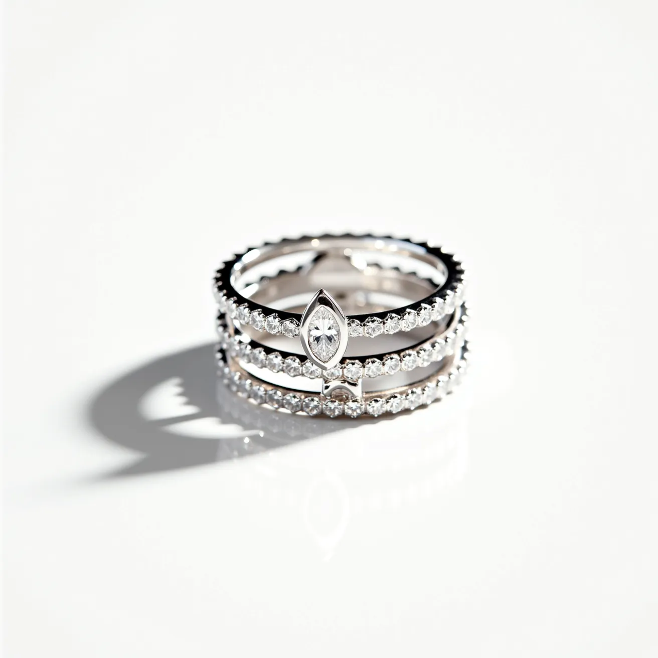 These stackable rings are crafted from a polished silver metal, featuring a series of small, round-cut diamonds set into each band. The uniformity of the gems suggests a prong setting, allowing for the maximum brilliance of each stone to be displayed. One of the rings is adorned with a larger, marquise-cut diamond set prominently within a bezel setting, adding a distinctive focal point to the stacked ensemble. The rings appear to fit seamlessly together, creating a cohesive and elegant look.