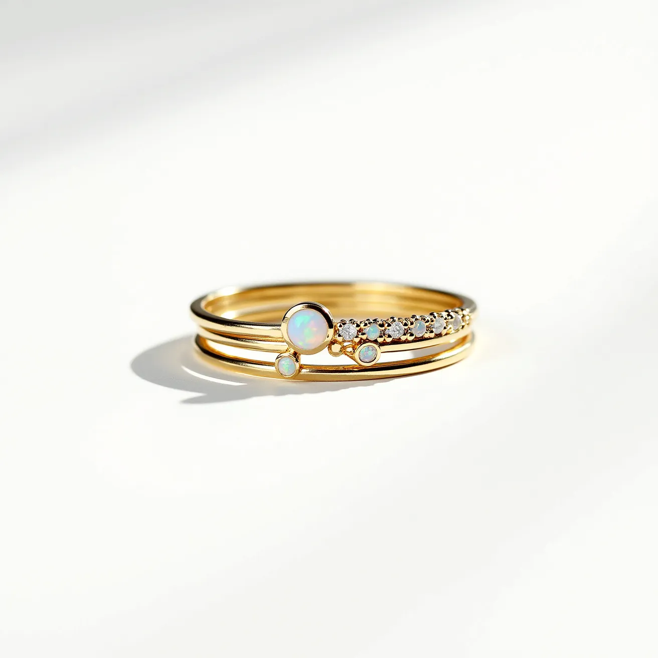 These stackable rings feature delicate bands crafted from a gold material, each carrying its own distinct charm. The first band is adorned with a prominent round opal set in a bezel setting, exhibiting a striking array of colors. Accompanying this opal are smaller opals, enhancing the ring's elegance. The second band showcases a series of small, round-cut gemstones, likely diamonds or cubic zirconias, set delicately across the top in a prong setting. The fine craftsmanship allows these rings to be worn together or separately, offering versatile styling options.