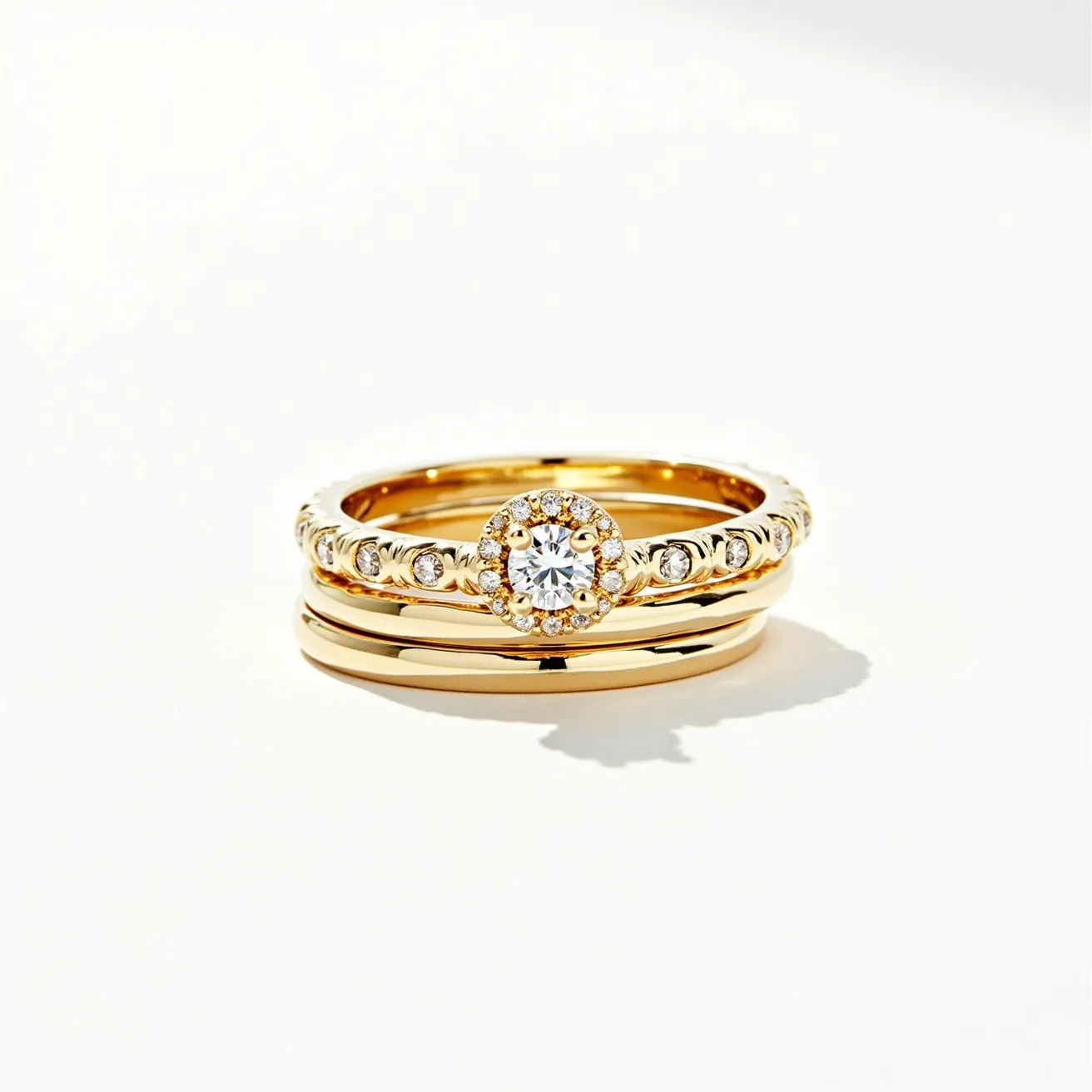 These stacked wedding rings feature a blend of elegant design and classic materials. The set comprises three bands, all crafted from lustrous yellow gold. The top ring is adorned with a prominent round-cut diamond, set securely in a halo setting that enhances its brilliance with a circle of smaller diamonds encircling the center stone. The middle band is elegantly detailed with a series of bezel-set round diamonds, adding a subtle sparkle. The final band is a simple, polished gold band, providing a timeless and versatile complement to the more ornate rings. The combination of these elements creates a harmonious and sophisticated look.