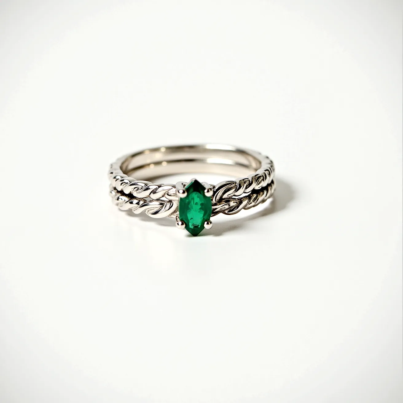 These stacked wedding rings feature a beautifully intricate design crafted from shiny silver material. The rings have a braided band that adds texture and elegance. The centerpiece is a striking marquise-cut green gemstone, set securely in a four-prong setting, which highlights its deep color and unique shape. The rings complement each other seamlessly, with one ring serving as a base and the other showcasing the gemstone, creating a harmonious and stylish ensemble.