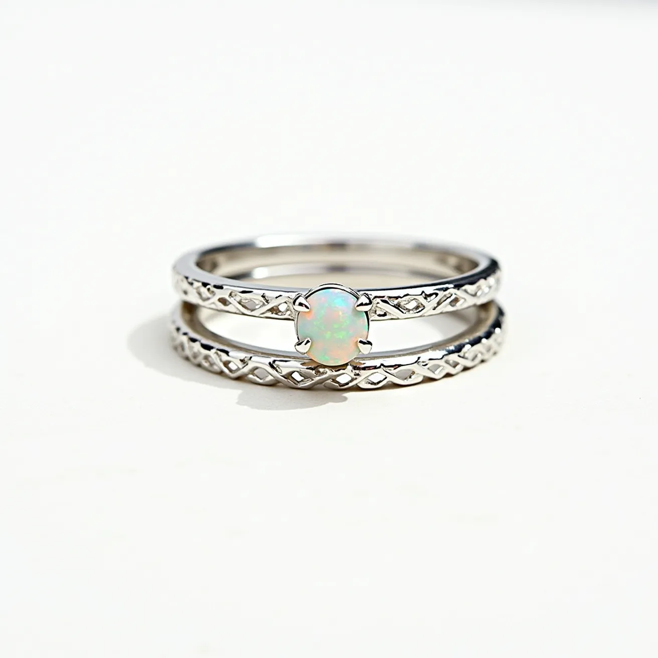 These stacked wedding rings are crafted from a glossy silver material, showcasing intricate detailing along their bands. The top ring prominently features an opal gemstone, cut in an oval shape and set in a four-prong setting, accentuating its iridescent beauty. The design presents a harmonious blend of elegance and artistry, with both bands complementing each other through a consistent pattern etched in the metal. The rings are designed to seamlessly fit together, highlighting both form and function in their attachment.