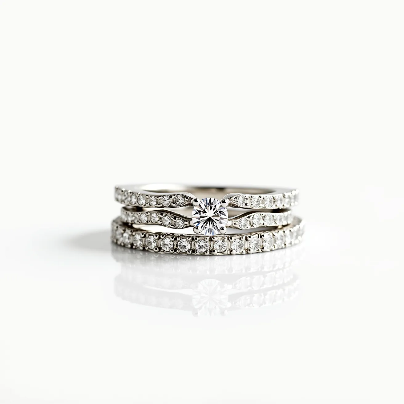 These stacked wedding rings feature a sophisticated design with multiple bands crafted from a shiny metal, likely white gold or platinum, offering a sleek and elegant appearance. The centerpiece ring showcases a sparkling round-cut diamond in a prong setting, which accentuates its brilliance and stands out. Surrounding this central piece, the rings are adorned with smaller round diamonds, set in a pave or channel setting, adding a continuous shimmer throughout the ensemble. The overall design is harmonious and unified, creating an exquisite appearance when the rings are stacked together.