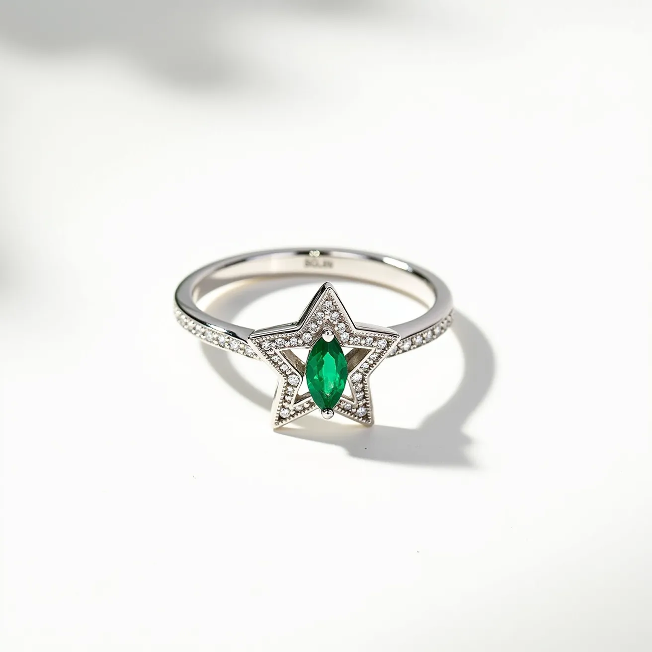 This star ring is a striking piece featuring a central marquise-cut green gemstone, likely an emerald, set prominently at the heart of a star-shaped design. The star is beautifully adorned with small round-cut clear stones, possibly diamonds, in a pave setting that enhances the ring’s brilliance and elegance. The band of the ring appears to be made of a polished silver or white gold material, which provides a sleek and sophisticated backdrop for the intricate stonework. The overall design emphasizes symmetry and sparkle, making it a captivating accessory.