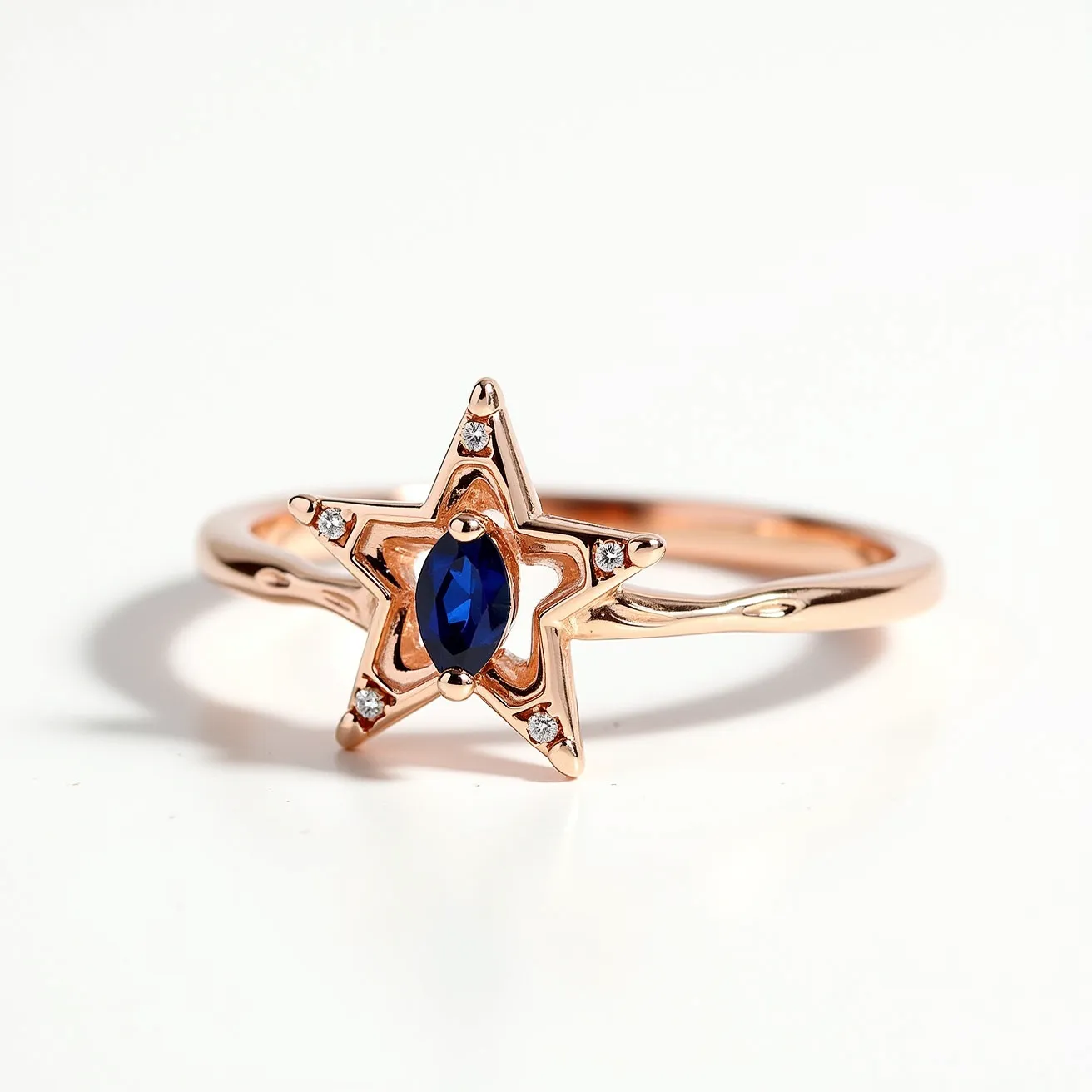 This star ring features a delicate rose gold band and a distinctive star-shaped setting. At the center, there is an oval-cut blue sapphire, held securely with four prongs. The star is outlined with small round diamonds, each set in a bezel setting at the tips of the star, adding a touch of sparkle and elegance. The simplicity of the material choice and design emphasizes the vibrant color of the sapphire and the brilliance of the diamonds, while the rose gold provides a warm and luxurious backdrop.