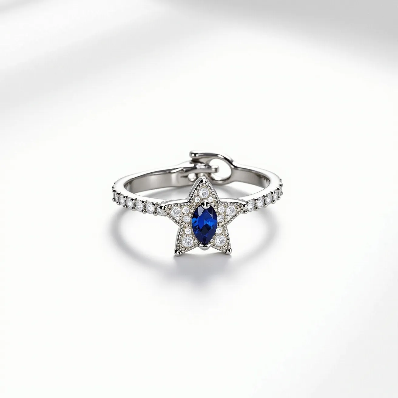 This star ring features a prominent star-shaped design embellished with a central marquise-cut blue gemstone, likely a sapphire, which is elegantly set in the center. The star's frame and the ring band are adorned with small, round clear stones, suggestive of diamonds or cubic zirconia, adding a captivating sparkle. The metals used for the ring appear to be a sleek, polished white metal, possibly white gold or platinum. The ring also has a delicate clasp or hinge design at the back, which adds a unique functional element to its structure. The combination of the deep blue centerpiece and the surrounding clear stones creates a striking contrast, enhancing the overall allure of the piece.