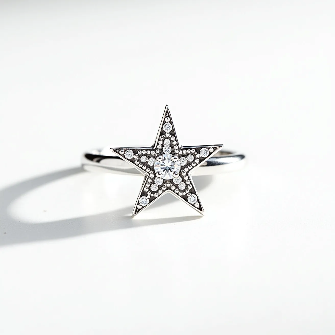 This star ring features a distinct design with its central motif shaped like a five-pointed star. The star is intricately adorned with a series of small, round-cut clear stones, likely diamonds or cubic zirconia, that are set along the edges, enhancing its sparkle. A larger, central stone sits prominently in the middle, possibly set in a prong or bezel setting to maximize its brilliance. The ring itself appears to be crafted from a reflective metal, such as white gold or sterling silver, which complements the clarity and brightness of the stones. The band is sleek and simple, drawing attention to the star design, with no visible clasps or additional attachments, indicating it’s a traditional closed shank ring, meant to slip onto the finger.