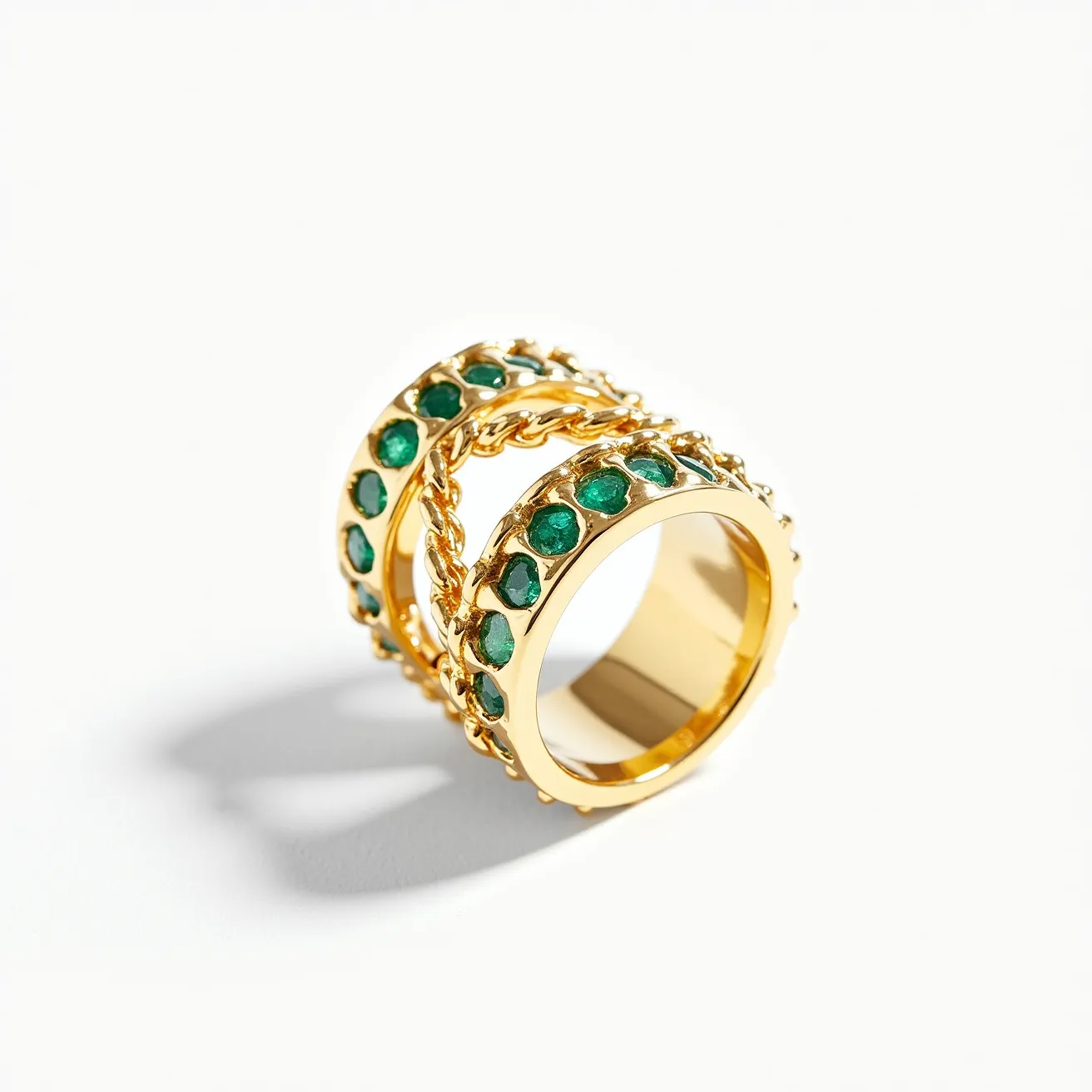 This statement ring is crafted from gold-toned metal and features two broad bands adorned with vivid green stones. The stones, likely round cut, are set in a continuous line, showcasing a rich, saturated hue that complements the gold. Between the bands, a delicate gold chain adds an intricate touch, creating a cohesive and elegant design. The setting of the stones is in a secure bezel style, ensuring both durability and a smooth finish. The ring's design is bold and luxurious, making it a striking accessory.