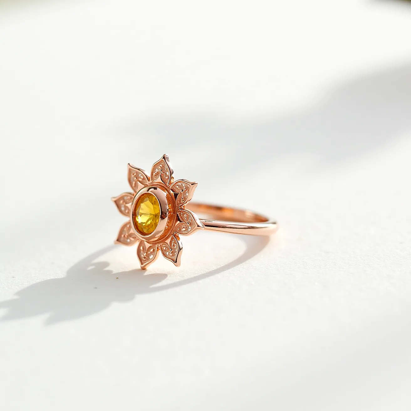 This sunflower ring features a finely crafted rose gold band, designed with an intricate sunflower motif. The centerpiece of the ring is a vibrant, oval-cut yellow gemstone, potentially citrine or a similar stone, set securely in a bezel setting that highlights its warm hue. The petals of the sunflower are skillfully detailed, adding a touch of elegance and artistry to the ring's design. The band appears smooth and polished, contributing to the overall sleek and graceful appearance of the piece, seamlessly integrating the floral theme with the luxurious material.