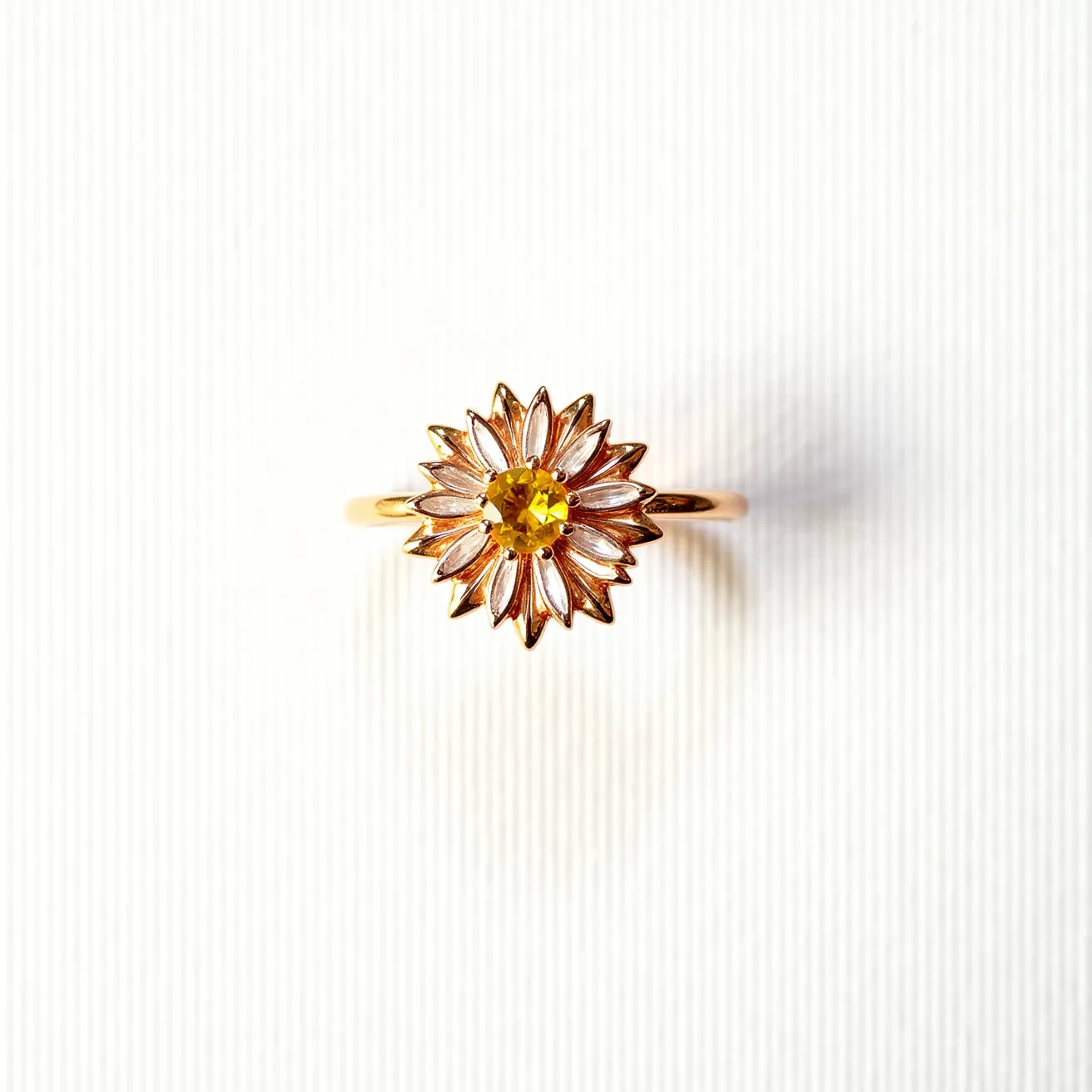 This sunflower ring is crafted from a gold-tone metal, designed to capture the vibrant and natural allure of a sunflower. At its center, a yellow gemstone is set in a prong setting, carved in a round cut, which sparkles brightly and symbolizes the core of the sunflower. The petals radiate outward, intricately detailed and highlighted by a shining finish, which adds depth and dimension to the piece. The band is designed to be simple and elegant, complementing the floral motif with a smooth and polished surface.