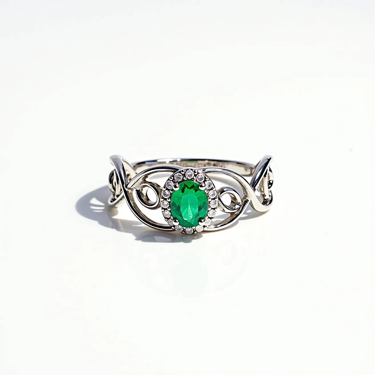 This tangled ring is crafted from a polished silver metal and features an intricate design that intertwines elegantly around the finger. At its center, an oval green gemstone, possibly an emerald, is prominent, adding a vibrant touch. The stone is set in a classic prong setting and encircled by a halo of small, sparkling clear stones that enhance its brilliance. The band showcases delicate loops and twists, creating a whimsical yet sophisticated look. There is no visible clasp or attachment mechanism as it is a continuous ring intended to slip onto the finger.