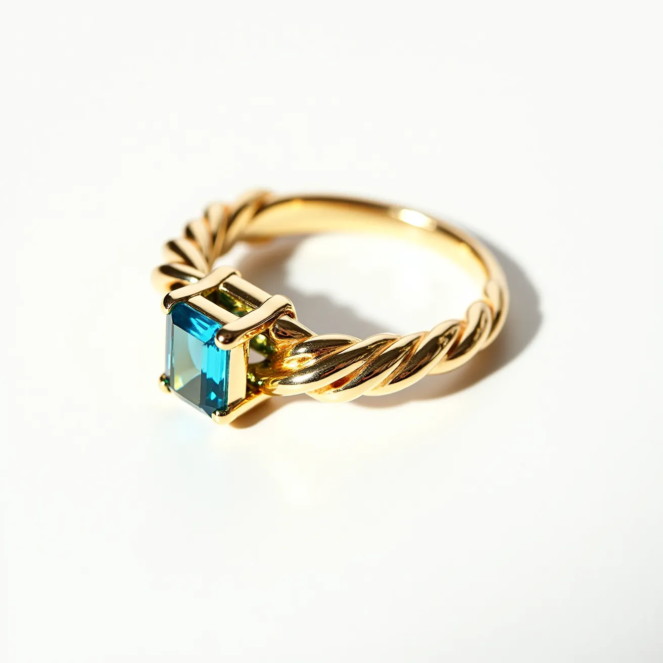 This tangled ring features a twisted band crafted from a polished gold material, adding an elegant and intricate texture to the piece. At the center, a striking blue gemstone is set, showcasing an emerald cut that enhances its clarity and depth. The gem is securely held in place by a four-prong setting, complementing the ring’s sophisticated design. The overall craftsmanship highlights a seamless blend of elegance and modernity.