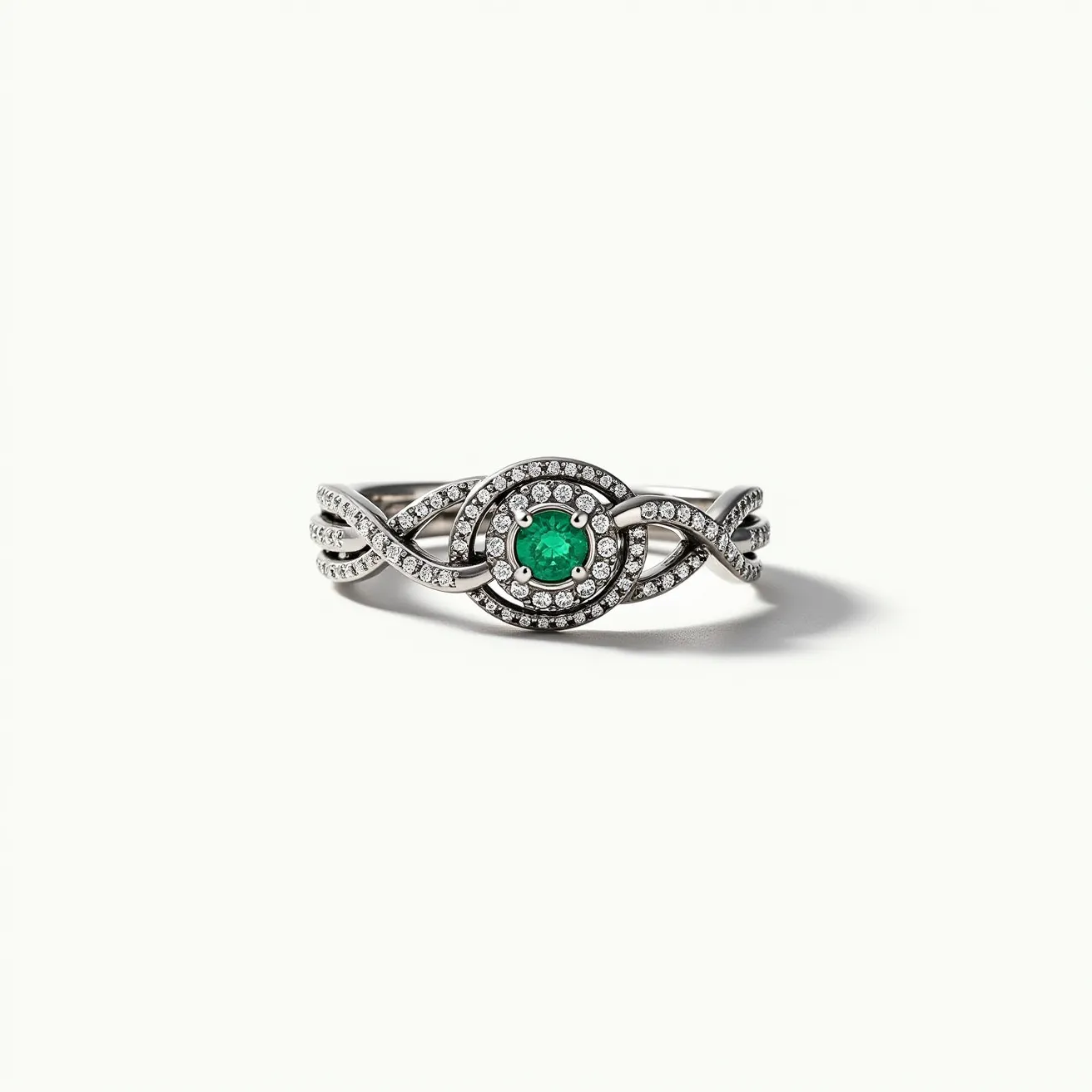 This tangled ring features an intricate design crafted from silver-colored metal interlacing bands, adorned with small, clear gemstones that are likely round-cut diamonds in a pavé setting. At the center, a vibrant green gemstone, possibly a round-cut emerald, is securely held in a four-prong setting, providing a striking focal point. The ring's twisted bands converge towards the central gem, enhancing the overall aesthetic with symmetry and elegance, with no visible clasp or attachment present.