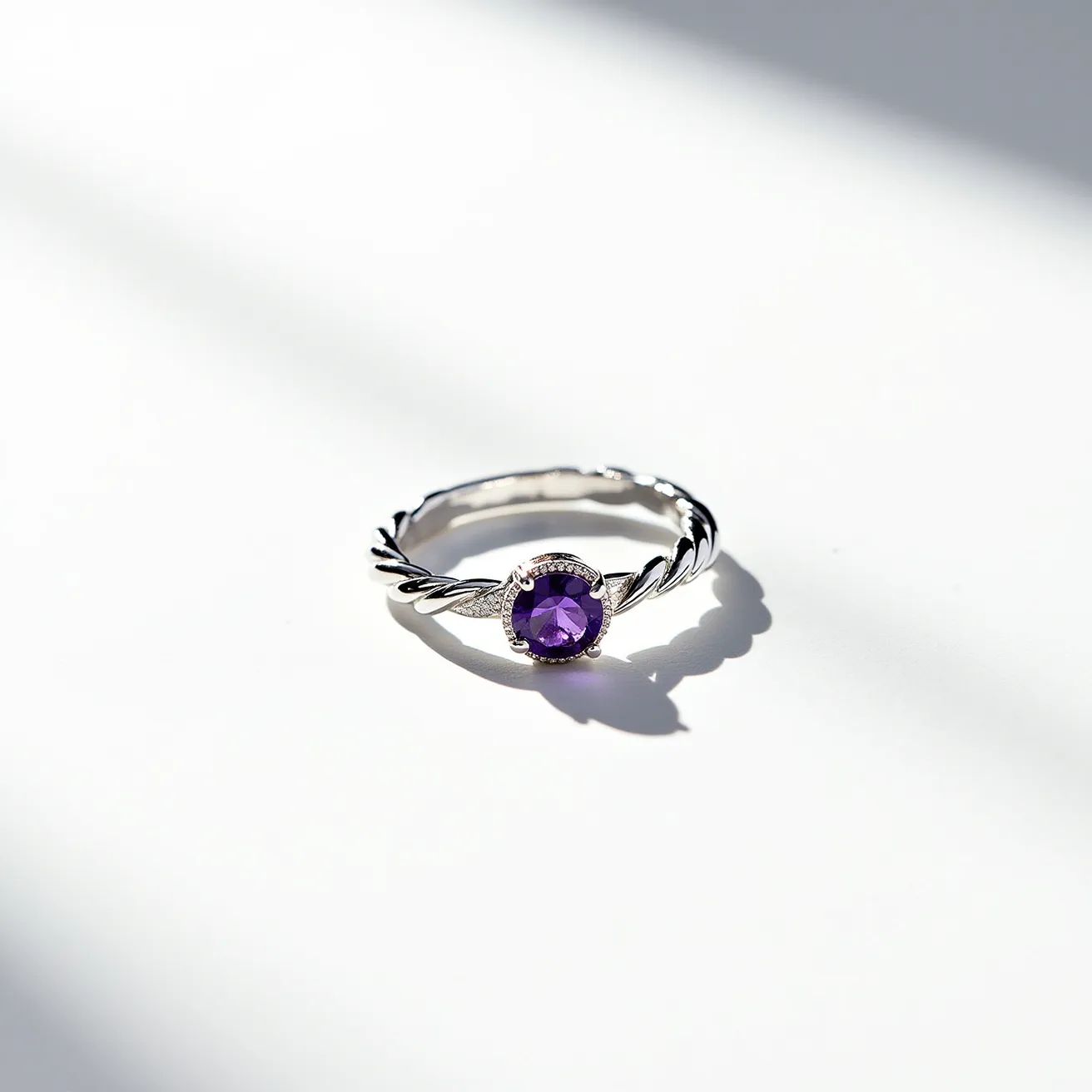 This tangled ring features a twisted band design crafted from a polished silver material. At its center, it holds a round-cut amethyst gemstone, securely set in a bezel setting that enhances its vibrant purple hue. The silver band has a rope-like texture, which adds an elegant yet simple touch to the overall design. There are no visible clasps or additional attachments, giving the ring a seamless appearance. The gemstone is the focal point, drawing attention with its rich, striking color set against the shiny silver backdrop.