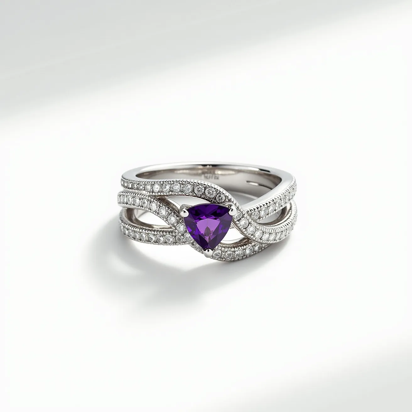 This tangled ring features a complex design crafted from a sleek silver or white gold band, intricately weaving to create an elegant and sophisticated appearance. At its center, the ring showcases a striking triangular-cut amethyst, held securely in place by a three-prong setting that enhances its vibrant purple hue. Surrounding the central stone are small, clear diamonds embedded along the intertwined band, each set in a delicate pavé setting, adding a layer of sparkle and luxury. The overall design brilliantly balances the boldness of the amethyst with the subtle shimmer of the diamonds, creating a stunning piece of jewelry with a timeless appeal.