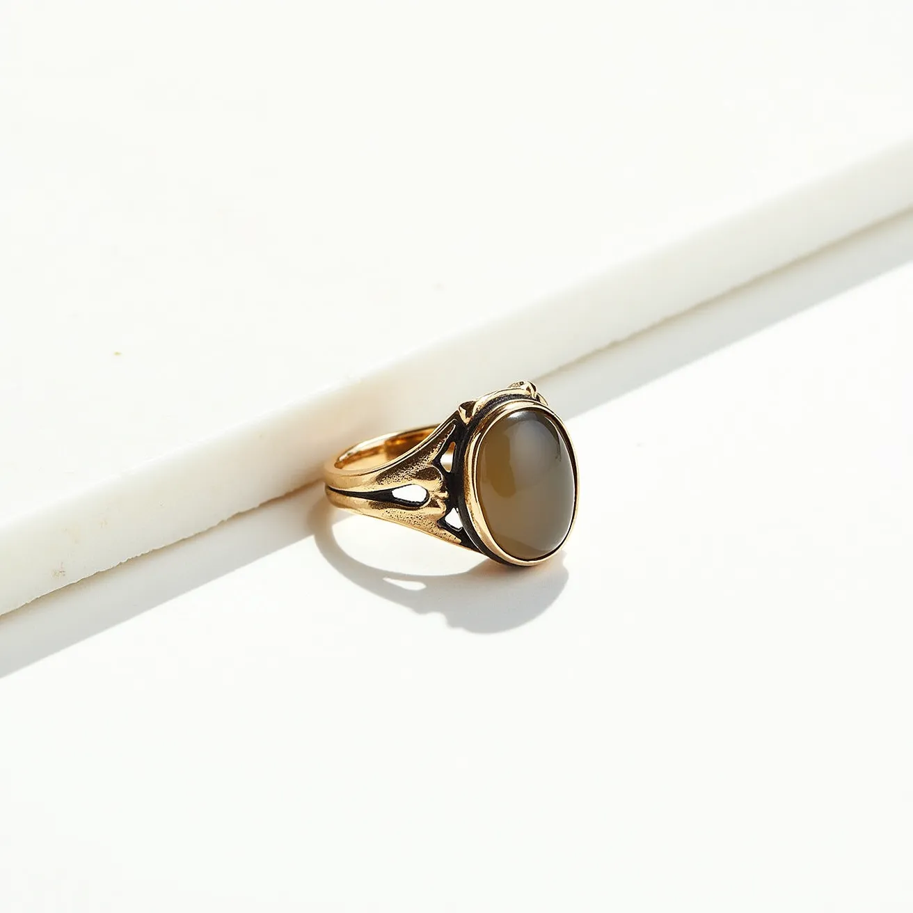 This thumb ring features a polished, gold-colored band with an intricate openwork design. The centerpiece is an oval-shaped, cabochon-cut stone, likely an agate or onyx, that is securely bezel set, providing a smooth, refined appearance. The polished finish of the metal contrasts elegantly with the muted sheen of the stone, creating a harmonious balance between the materials. The ring's construction shows a seamless integration of the band and stone setting, underscoring a high level of craftsmanship and attention to detail.