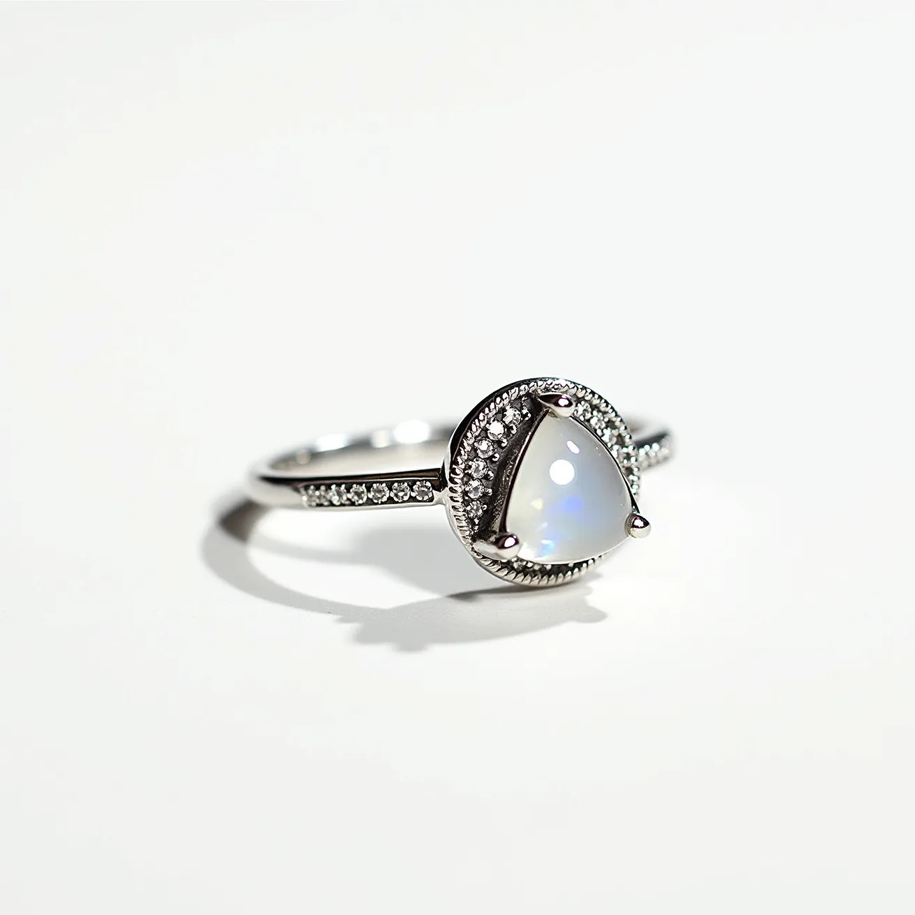 This thumb ring features a sleek silver band adorned with a central teardrop-shaped moonstone, known for its iridescent sheen. The moonstone is securely set with three prongs and surrounded by a halo of small, round-cut diamonds that add a sparkling accent to the design. The band is further embellished with a row of tiny diamonds, enhancing the elegant and luxurious appearance of the ring. The combination of gemstones and metalwork reflects a modern yet timeless aesthetic.