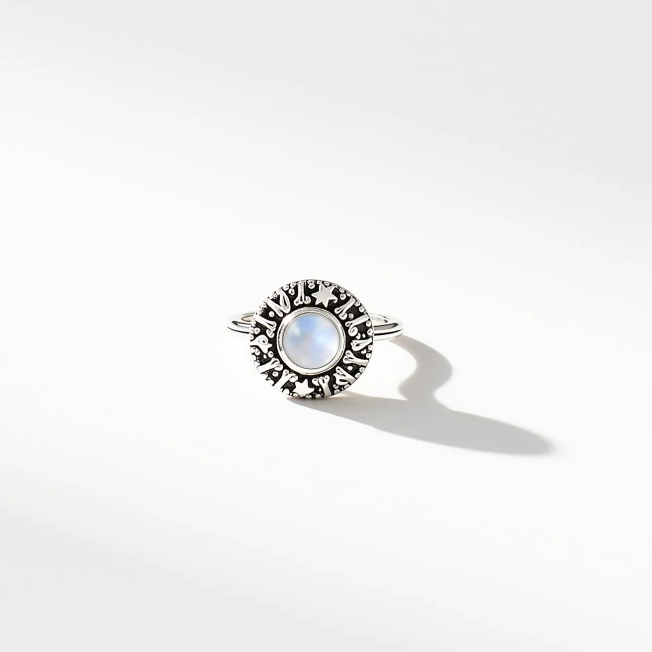 This thumb ring features a round, polished moonstone set centrally within a detailed silver band. The stone is cabochon cut, enhancing its natural opalescent qualities. Surrounding the moonstone is an ornate silver bezel with intricate engravings, adding a touch of elegance and complexity to the design. The double band enhances stability and style, ensuring a comfortable fit. There are no clasps or additional attachments, emphasizing the simplicity and sophistication of the piece.