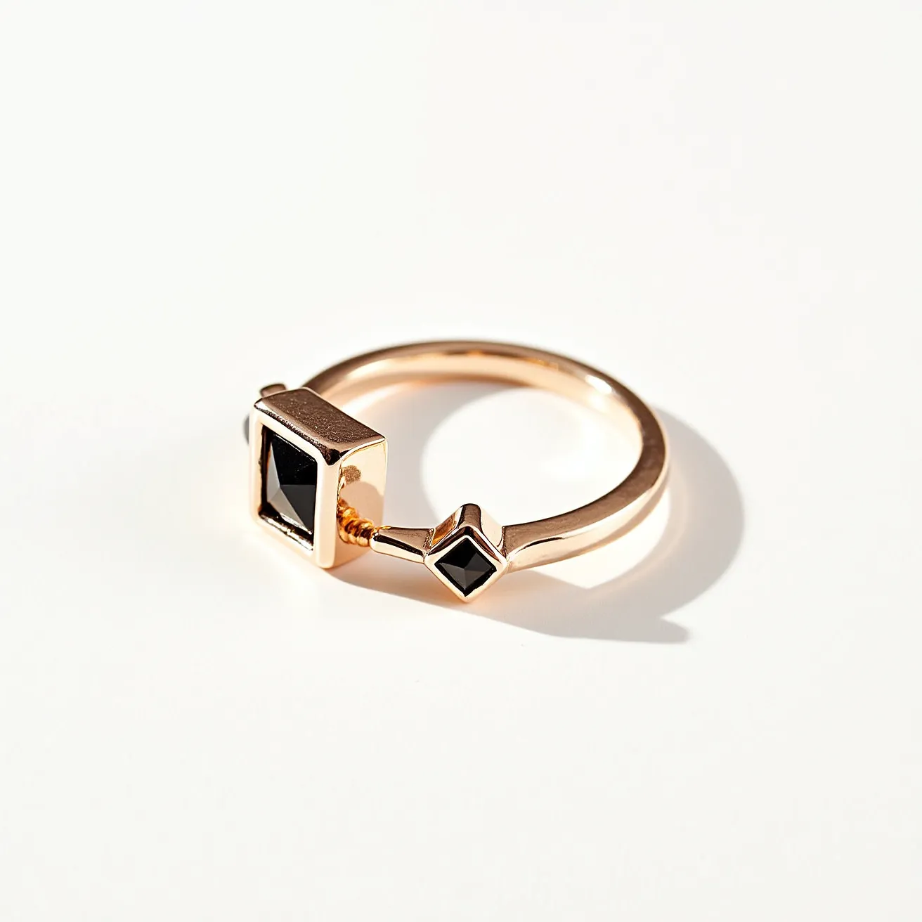 This thumb ring features a sleek, polished band made of a metal that appears to be rose gold. It showcases two striking black stones. The larger stone is set in a rectangular bezel setting, and the smaller stone is elegantly positioned in a square bezel. The geometric design enhances the modern aesthetic of the ring. The stones are likely onyx or black diamonds, adding a bold contrast to the warm tone of the metal. The unique design makes it a distinctive accessory for any occasion.