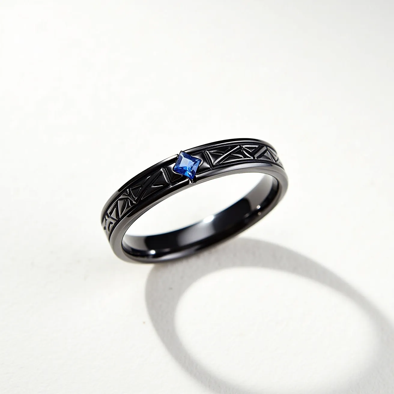 This tungsten ring features a sleek, dark metallic band intricately engraved with geometric patterns. It prominently showcases a small, square-cut blue gemstone, securely set in a bezel setting at the center of the band. The design details enhance the ring's modern and distinctive appearance, complementing the deep color of tungsten with the vibrant blue of the gem. The absence of clasps or attachments ensures a seamless and smooth finish, highlighting the craftsmanship and style of the piece.