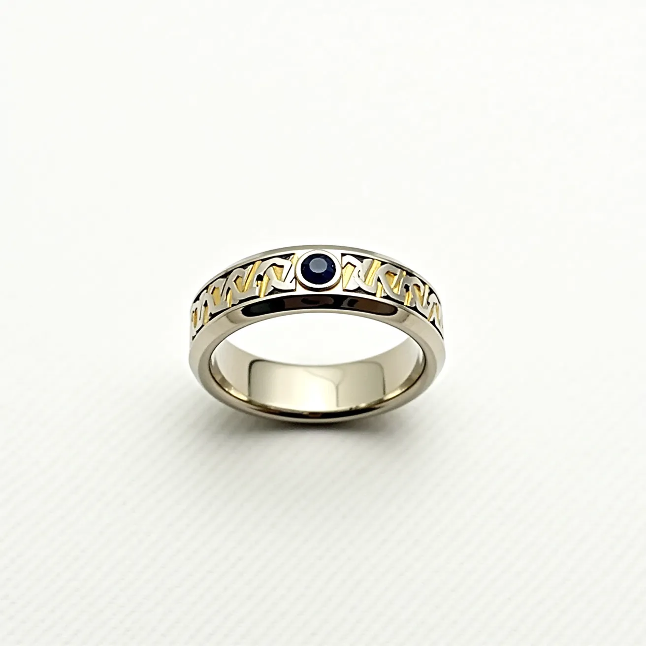 This tungsten ring features a sleek, polished finish with intricate gold-colored detailing that creates an elegant pattern encircling the band. At the center, a round, dark blue gemstone is neatly set in a bezel setting, adding a striking contrast to the ring's metallic sheen. The combination of durable tungsten with the luxurious appearance of the gold accents and the deep color of the gem creates a sophisticated and distinctive piece of jewelry.