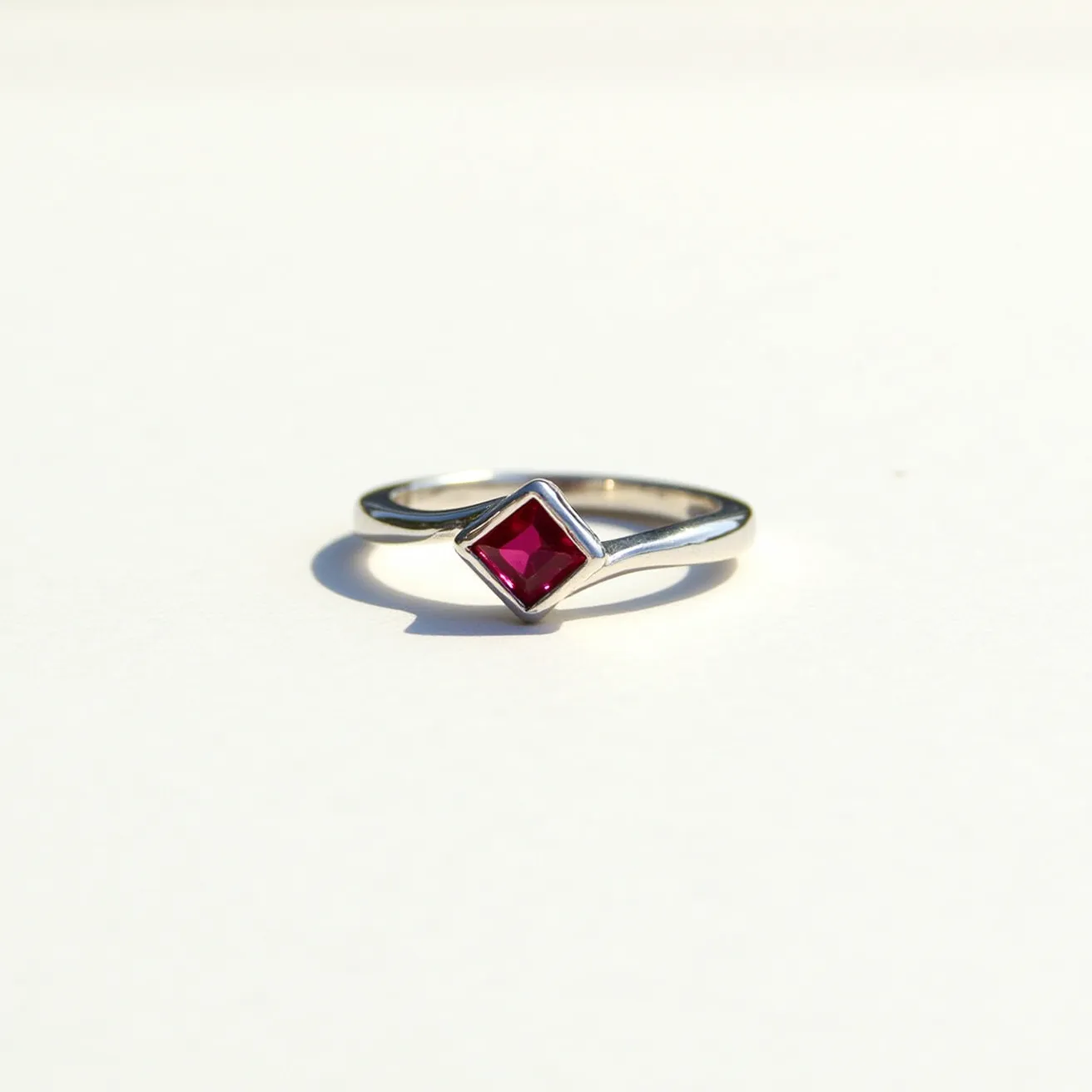 This two birthstone ring features a sleek, polished metal band, likely made of sterling silver or white gold, giving it a bright metallic sheen. The ring holds a single square-cut gemstone in a bezel setting, showcasing a vibrant red hue, which may suggest it is a garnet or a ruby, traditional birthstones for January or July. The design is simple and elegant, with clean lines that highlight the luster of the metal and the brilliance of the stone. The lack of additional ornamentation ensures focus remains on the radiant gem and the refined structure of the ring.