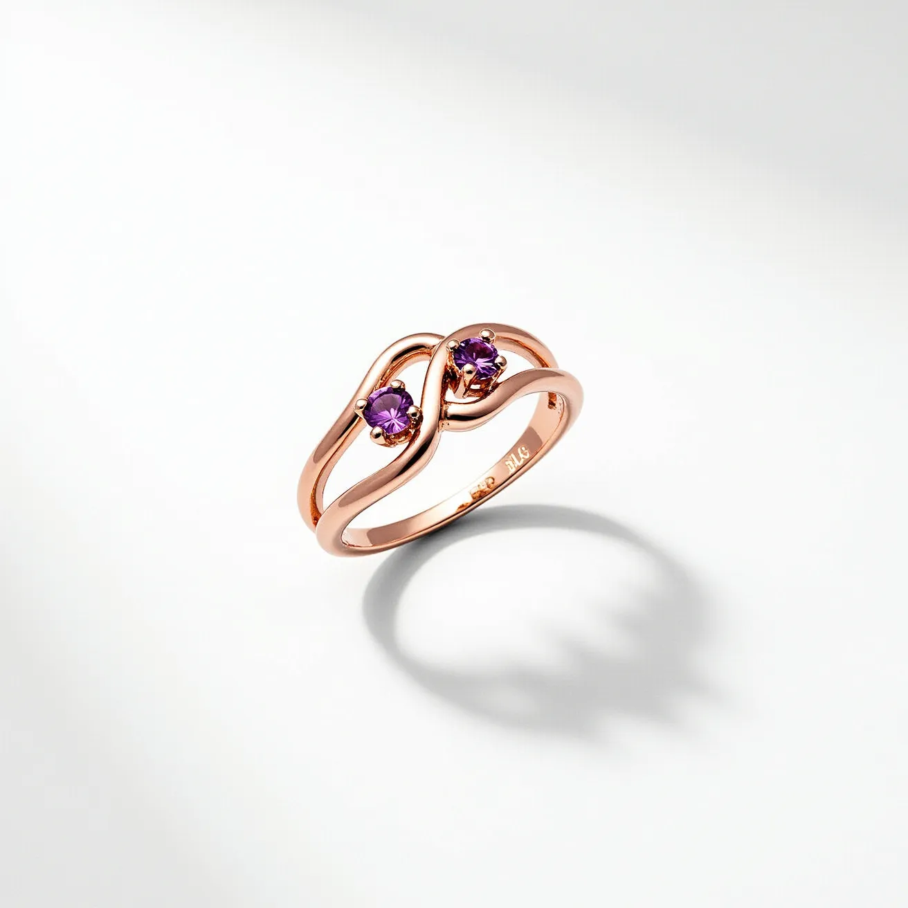 This two birthstone ring features a gracefully intertwined design crafted from rose gold. The ring showcases two round-cut amethyst gemstones, each securely held in place by a four-prong setting. The elegant curves of the band highlight the vibrant purple hue of the amethysts, creating a harmonious and sophisticated appearance. The ring’s open band and seamless construction emphasize its delicate and modern aesthetic, with no visible clasp or additional attachments.