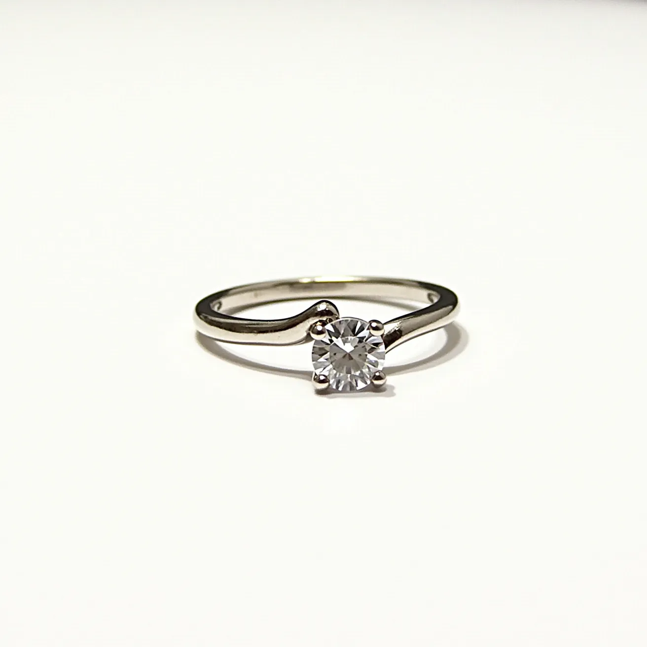 This vine engagement ring features an elegantly curved band, seemingly crafted from a polished metal that reflects a sophisticated and understated brilliance. At the center of this design is a round-cut gem, possibly a diamond, held securely by a four-prong setting that enhances its sparkle and draws attention to its clarity and radiance. The band’s graceful vine-like curvature provides an organic aesthetic that complements the gem's classic cut, creating a harmonious balance between nature-inspired design and traditional elegance. This ring’s simplicity and refined details make it a timeless piece suitable for a meaningful occasion.