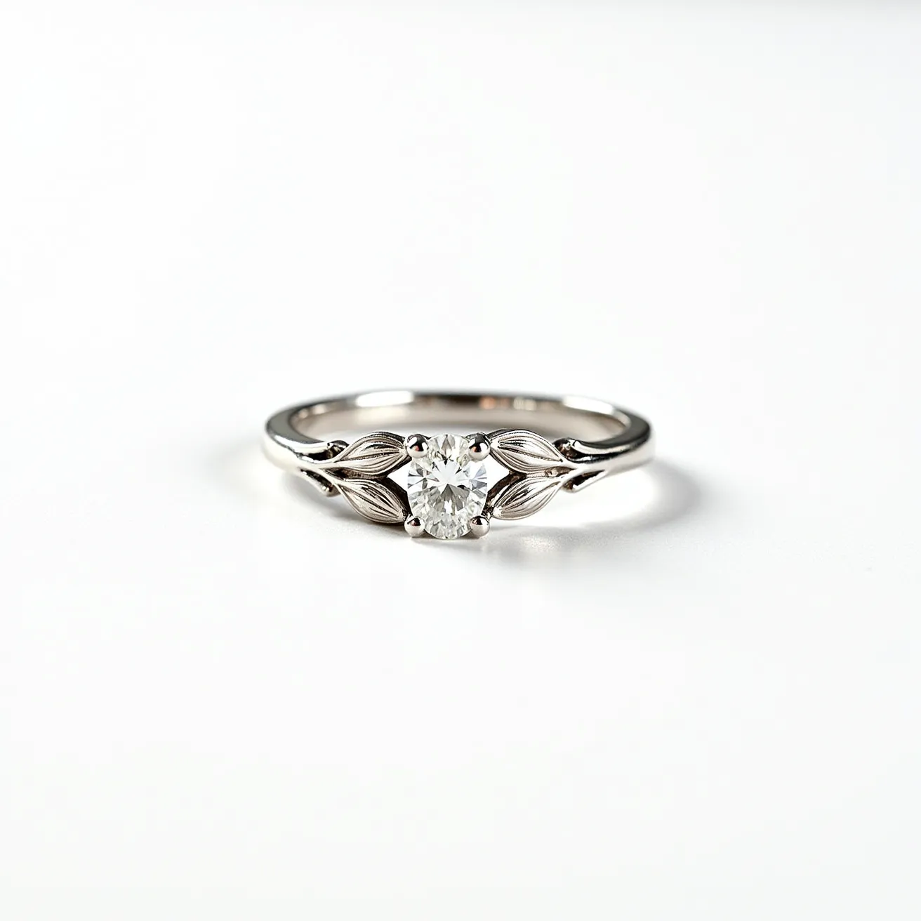 This vine engagement ring features a delicate design with a prominent round-cut diamond set at its center. The band appears to be made of a polished white metal, likely platinum or white gold, which complements the sparkle of the diamond. The metal band incorporates intricate vine motifs with leaf-shaped details that enhance its natural elegance. The central diamond is securely held in place by a classic four-prong setting, which allows ample light to pass through and maximize its brilliance. The overall design combines nature-inspired elements with timeless sophistication, making it an exquisite choice for symbolizing eternal love.