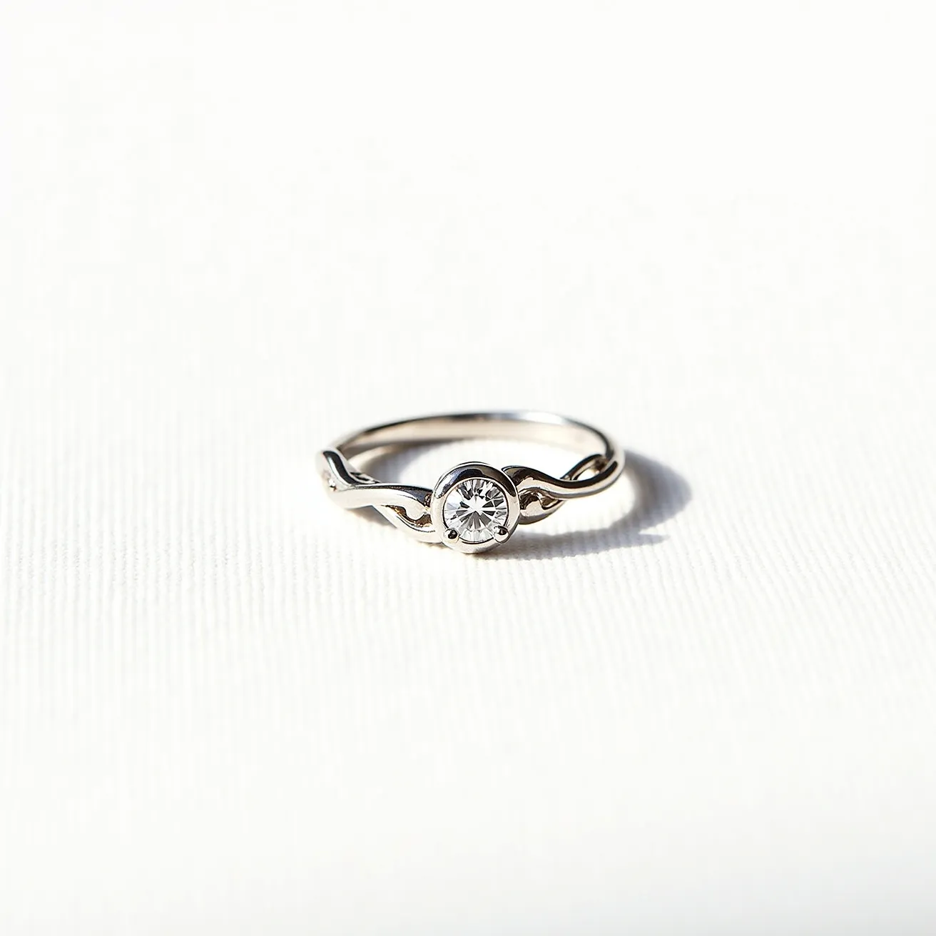 This vine engagement ring features a delicate intertwining band, crafted from what appears to be a polished metal, likely white gold or platinum, designed to mimic the elegance of a natural vine. At its center is a single round-cut diamond held securely within a bezel setting, allowing the gem to be showcased prominently while offering a modern twist on a classic solitaire design. The minimalist and nature-inspired aesthetic is both timeless and sophisticated, making it a perfect symbol of enduring love.