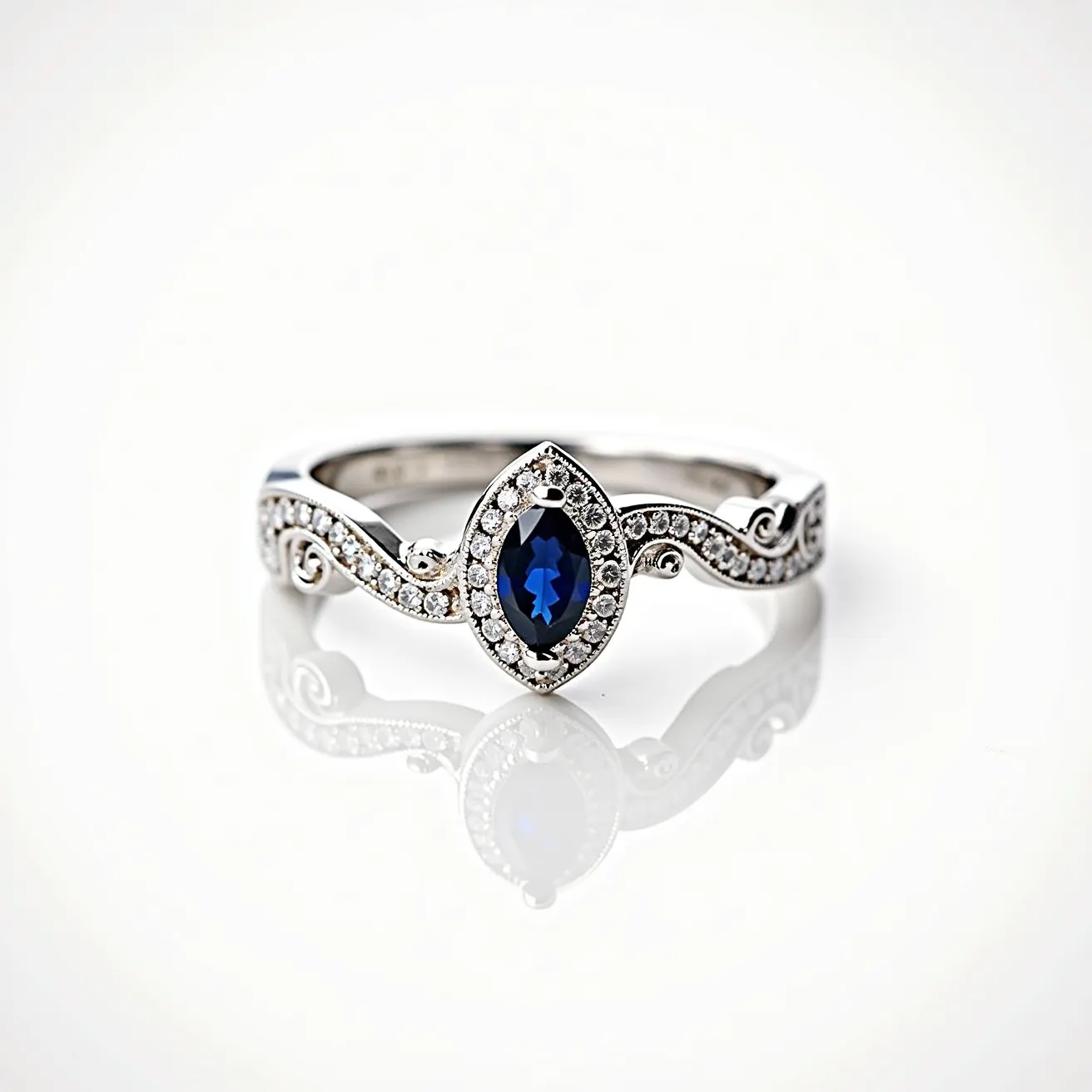 This vine engagement ring features a distinctive marquise-cut sapphire as its central gemstone, set securely within a halo of small, sparkling diamonds that enhance its vivid blue hue. The band is crafted from polished white metal, likely white gold or platinum, and is intricately designed with a vine motif that curves elegantly around the finger. The vine's tendrils are accentuated with additional small diamonds, adding brilliance and texture to the design. The ring combines both classic and nature-inspired elements, creating a unique and romantic piece of jewelry.