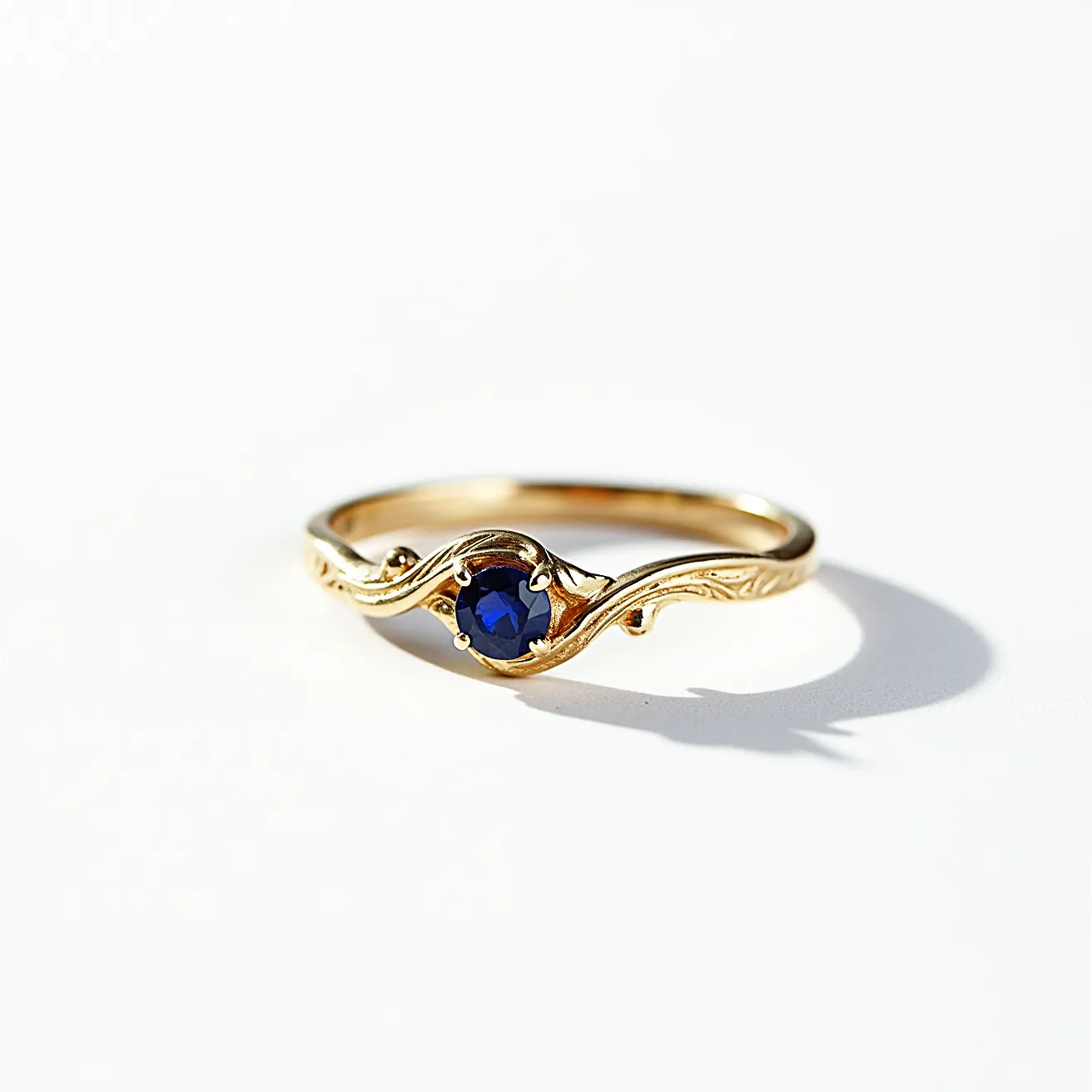 This vine engagement ring features a beautifully intricate design crafted in gold, embodying an elegant and nature-inspired aesthetic. At its center is a round brilliant-cut sapphire, securely set in a four-prong setting that enhances the stone's deep blue hue. The band is gracefully adorned with a vine motif, adding texture and a touch of whimsy to the piece. This combination of a vibrant gemstone and detailed metalwork makes the ring a unique symbol of love and commitment.