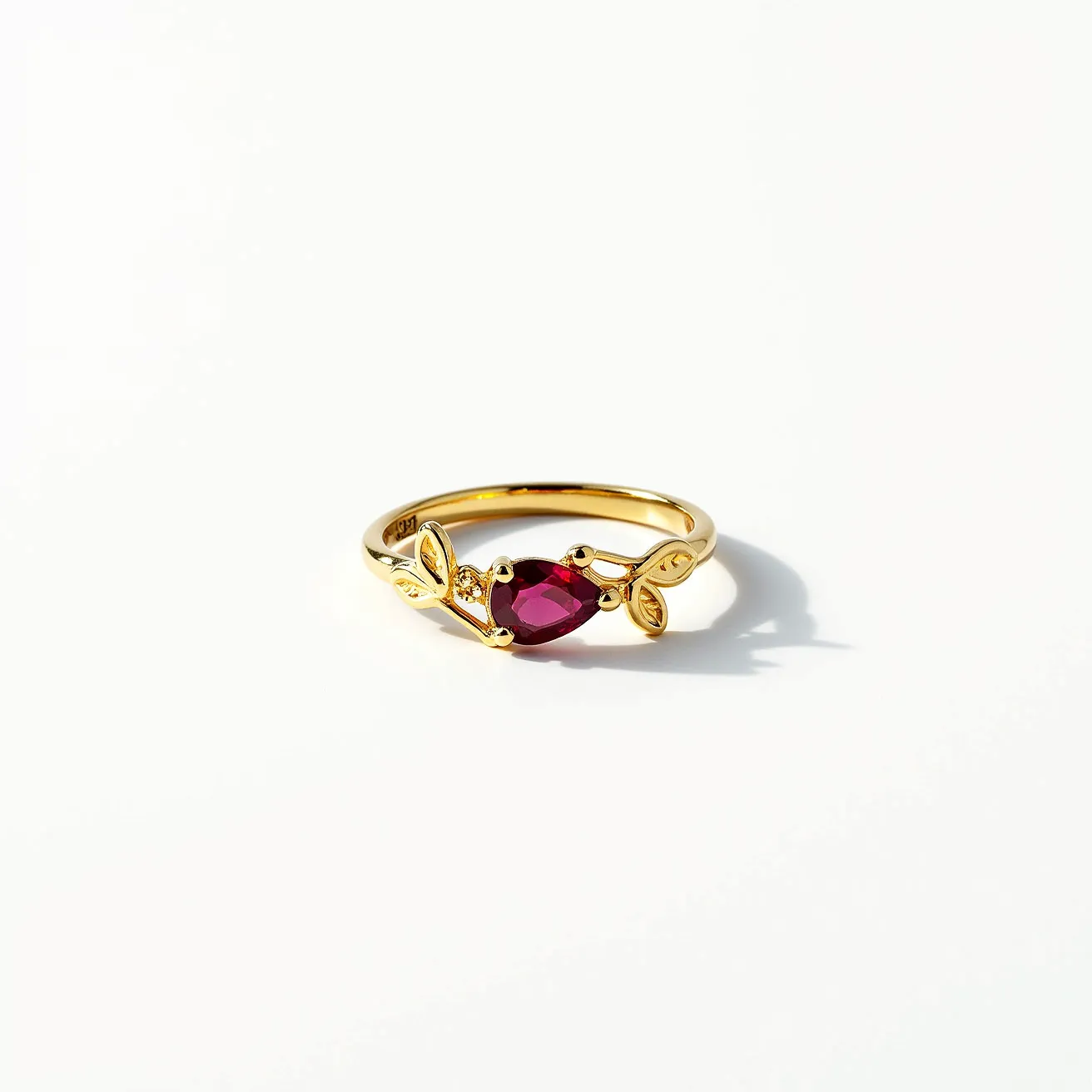 This vine ring features a delicate gold band adorned with leaf motifs, showcasing a striking pear-shaped ruby at its center. The ruby glistens with a deep red hue and is elegantly set in a prong setting, enhancing its visibility and capturing light beautifully. The gold leaves entwine gracefully around the central stone, adding an organic and intricate touch to the design. Crafted to resemble natural vine growth, this ring embodies a harmonious blend of nature-inspired elegance and refined craftsmanship.