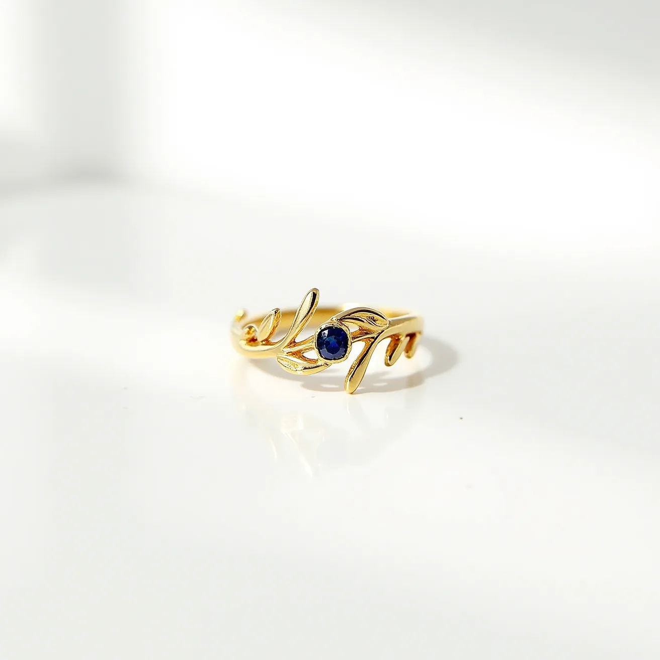 This vine ring is crafted from a gold-tone material featuring an elegant, twisting vine design. At its center, a small, round sapphire gemstone is delicately set. The stone, with its deep blue hue, is held in place by a simple bezel setting, allowing it to sit gracefully amidst the swirling vine motif. The ring does not exhibit any visible clasps, emphasizing its continuous, organic form that symbolizes natural beauty and elegance.