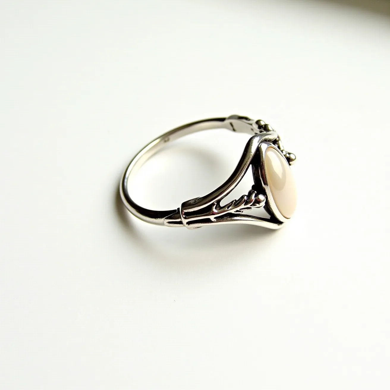 This vine ring features a sleek metal band, possibly made of silver or a similar lustrous material, intricately designed with vine-like embellishments that wrap around the band. It prominently showcases an oval-shaped stone, set in a bezel setting, adding an elegant and smooth focal point to the piece. The stone appears to have a polished, opaque surface with a creamy hue, enhancing its understated beauty. The ring's flowing design and carefully placed elements highlight its craftsmanship and aesthetic appeal.