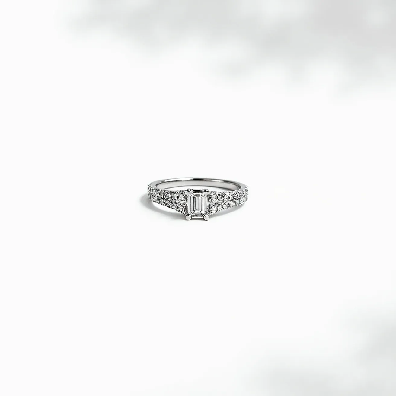 This wedding band features a central rectangular step-cut gemstone, likely an emerald cut diamond, set in a classic prong setting. The band is made of a polished metal, probably platinum or white gold, offering a sleek and elegant appearance. The shoulders of the band are adorned with smaller round-cut diamonds in a pavé setting, adding extra sparkle and enhancing the overall brilliance of the design. The combination of these elements creates a timeless and sophisticated look suitable for a wedding ring.