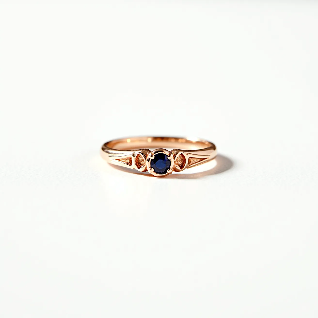 This wedding band is crafted from a warm, rose gold material, exhibiting an elegant and classic design. It features a central sapphire gemstone, displaying a deep blue hue, cut into a round shape. The stone is securely set in a bezel setting, enhancing its visibility and protection within the band. The design includes delicate, engraved patterns on either side of the central stone, adding to the ring's intricate and sophisticated aesthetics. The overall craftsmanship of the band showcases both simplicity and refinement, with a seamless finish.