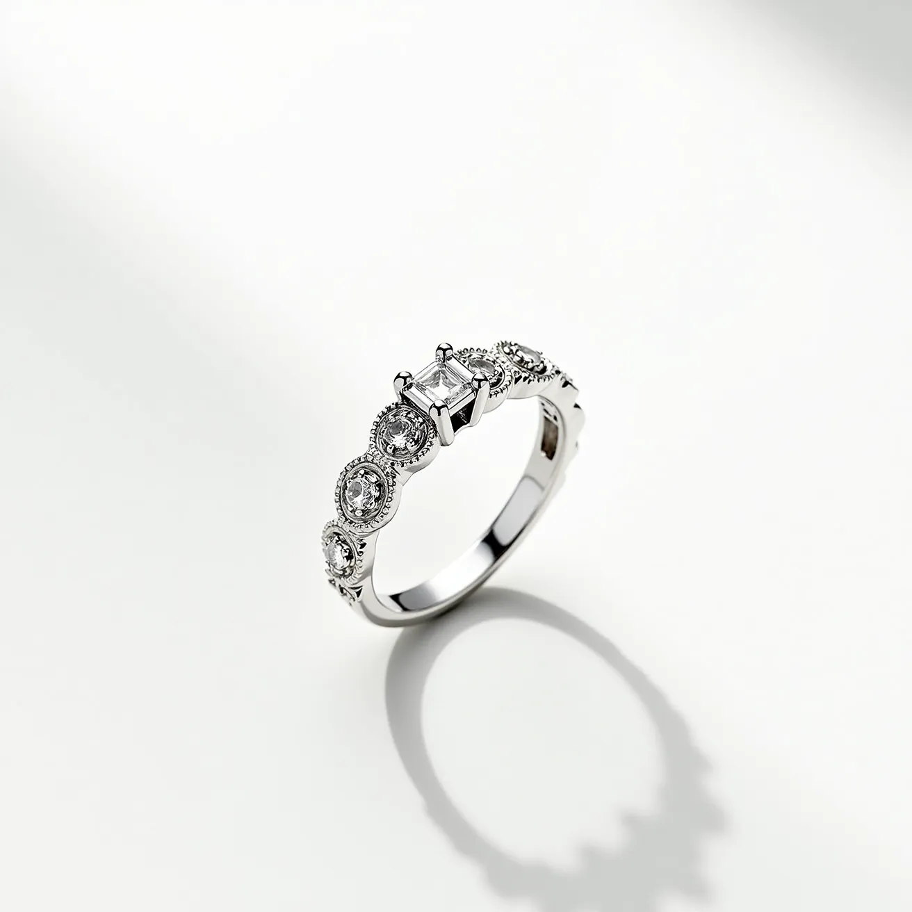 This wedding ring features a elegant design crafted from a white metal that appears to be platinum, showcasing a central square-cut diamond in a prong setting, ensuring it captures light beautifully. Surrounding the central stone, round diamonds are each set in intricate milgrain bezels, adding a touch of vintage sophistication. The band has a continuous pattern, with stones that enhance the ring's radiant elegance. The design does not include a clasp or attachment, emphasizing its classic and seamless construction for everyday wear.